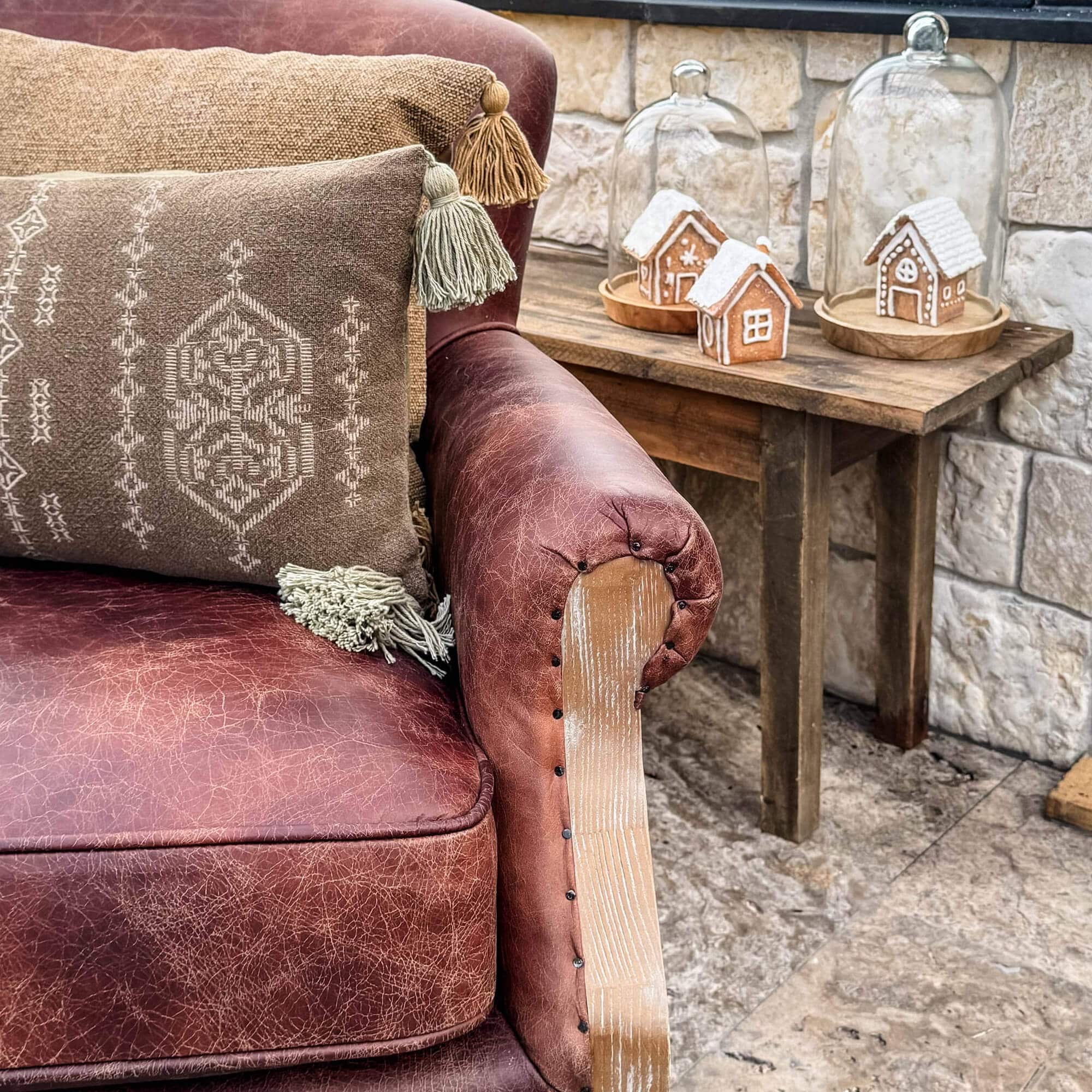 Braunes Ledersofa mit dekorativen Kissen und Holztisch mit Lebkuchenhäusern unter Glaskuppeln