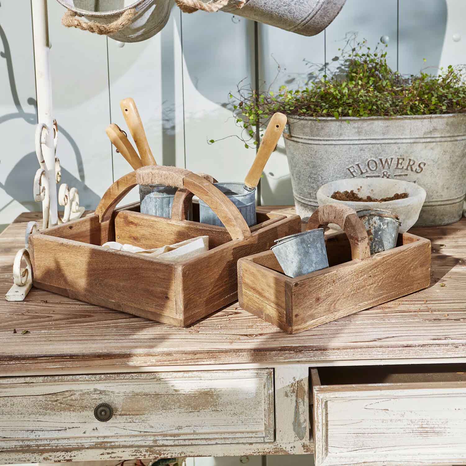 Holzkisten mit Griffen, gefüllt mit Gartengeräten und Metalltöpfen auf einem Holztisch
