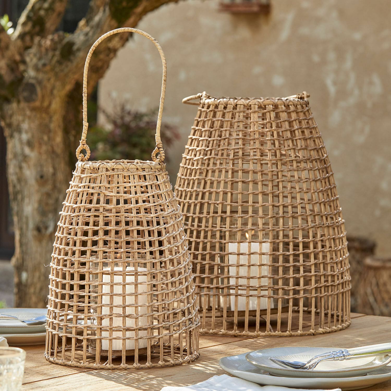 Laterne 2er Set Hillendale Zwei natürliche Rattan-Laternen mit weißen Kerzen auf einem Holztisch im Außenbereich