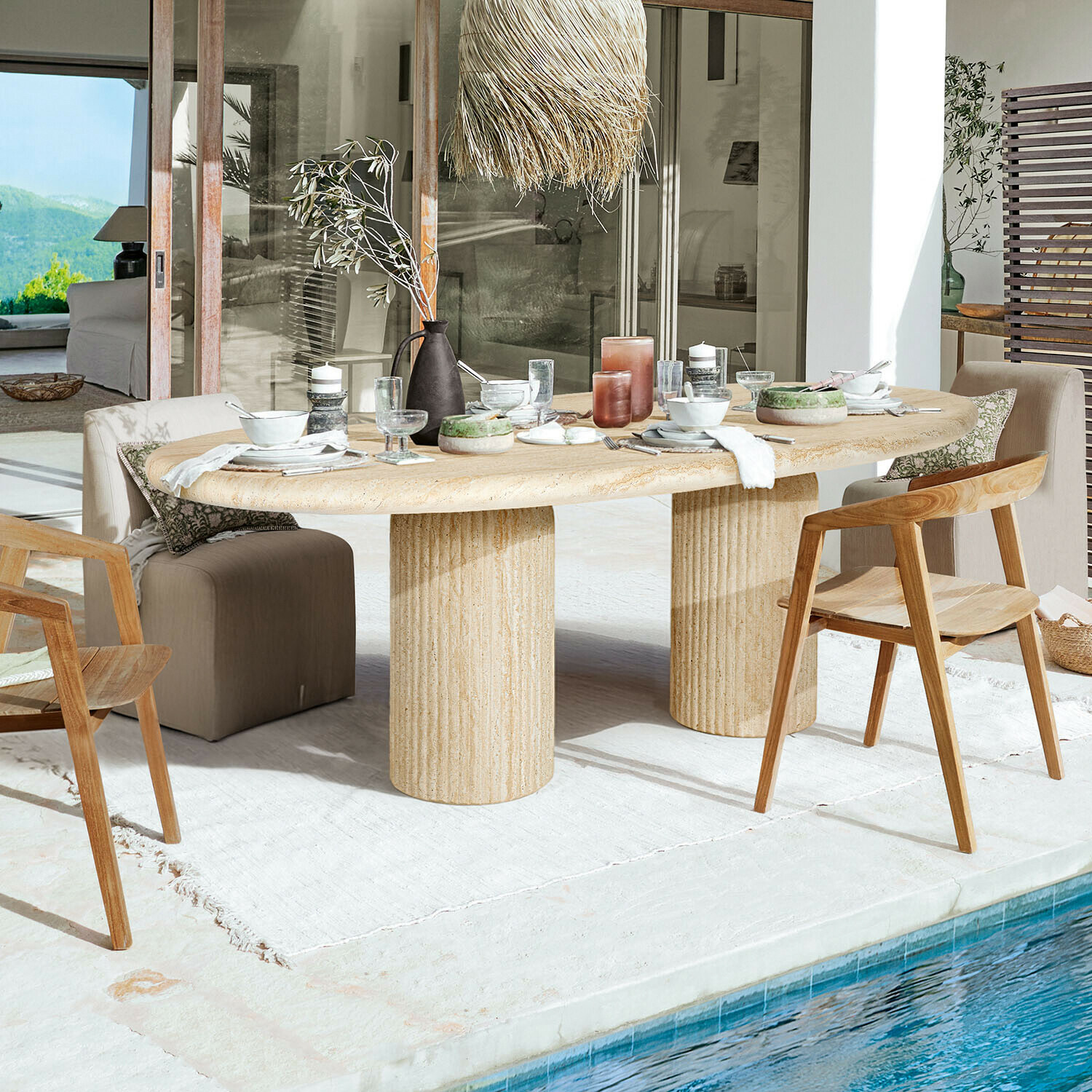 Tisch Calerio Ovaler Esstisch aus beigem Stein mit zwei zylindrischen Säulen auf Terrasse am Pool mit Holzstühlen