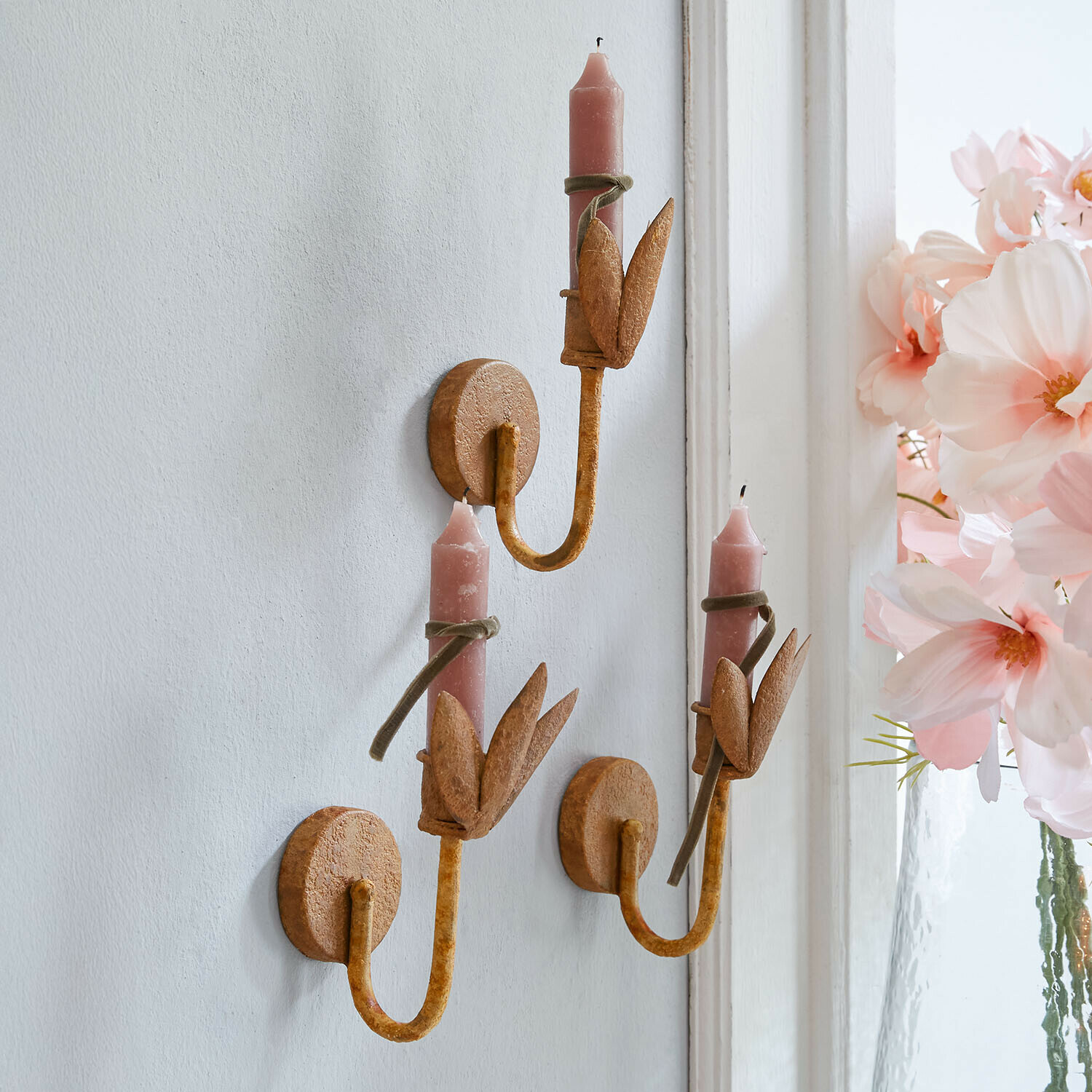 Set aus drei rostfarbenen Metall-Wandleuchtern mit rosa Kerzen und Blattdekoration