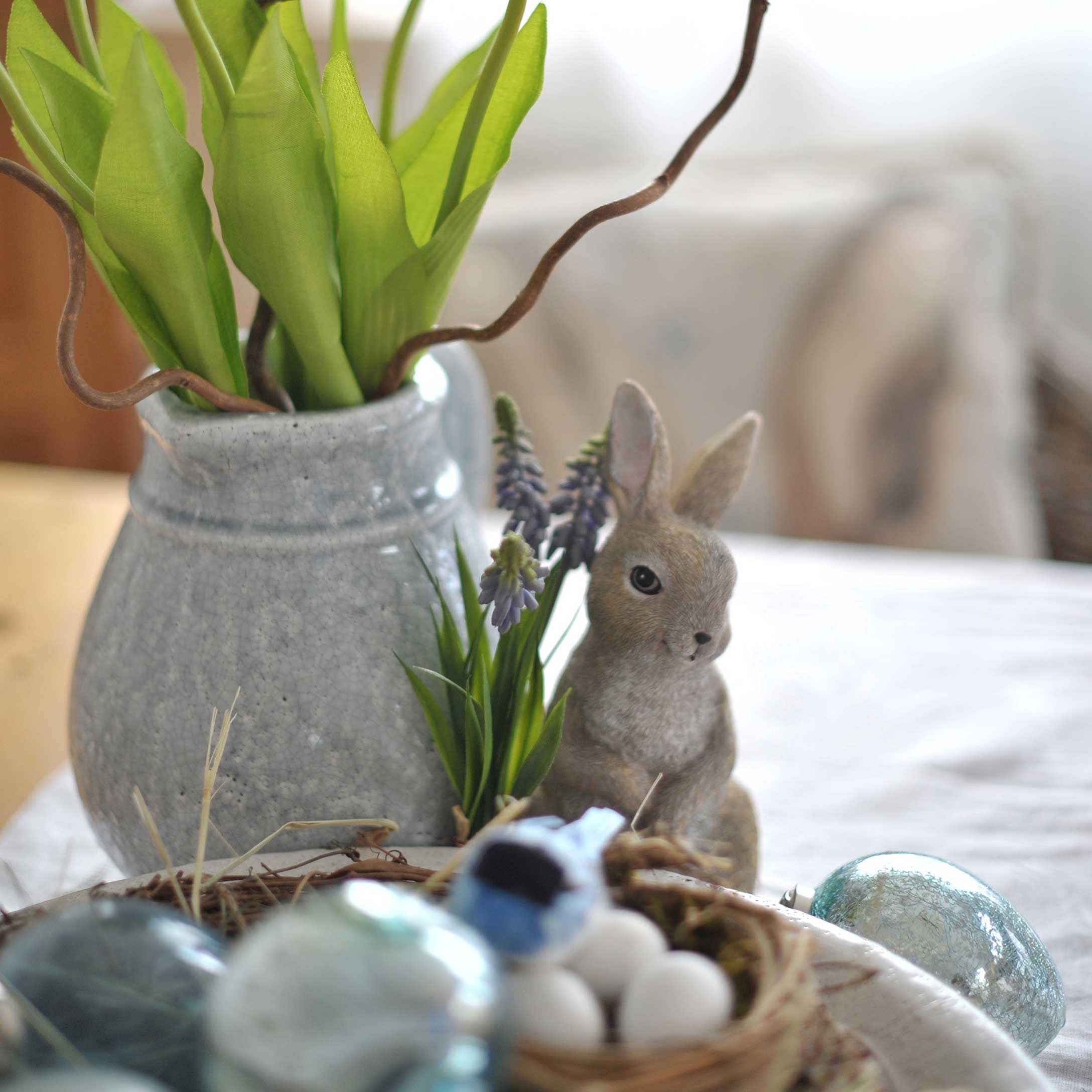 Grauer Keramikvase mit grünen Blättern und Hasenfigur als Osterdekoration auf Tisch