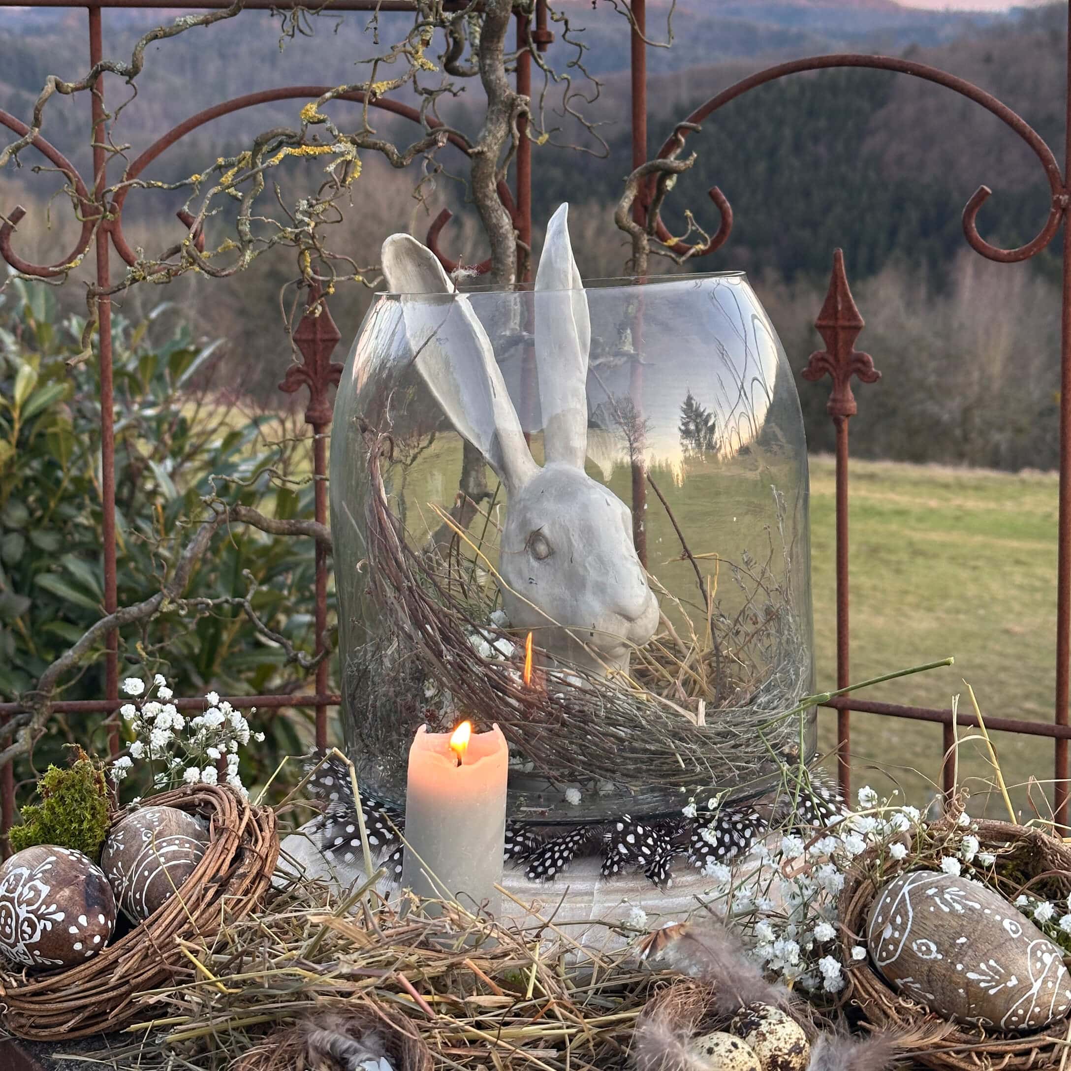 Natürlich dekorierte Osterfreude mit weißem Keramikhasen in Glasvase und brennender Kerze rustikal