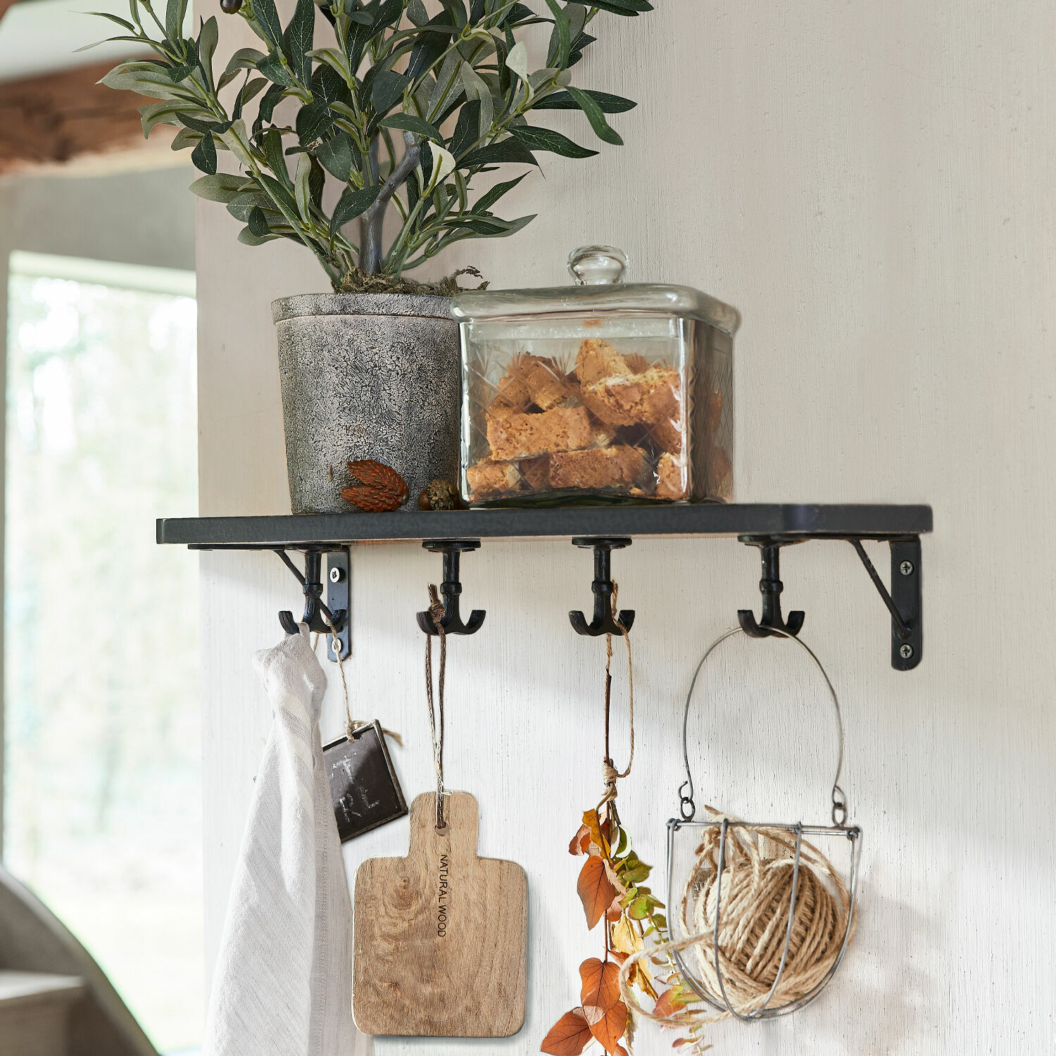 Wandregal Agnessa Schwarzes Metallwandregal mit Haken, Blumentopf und Glasdose mit Keksen darauf