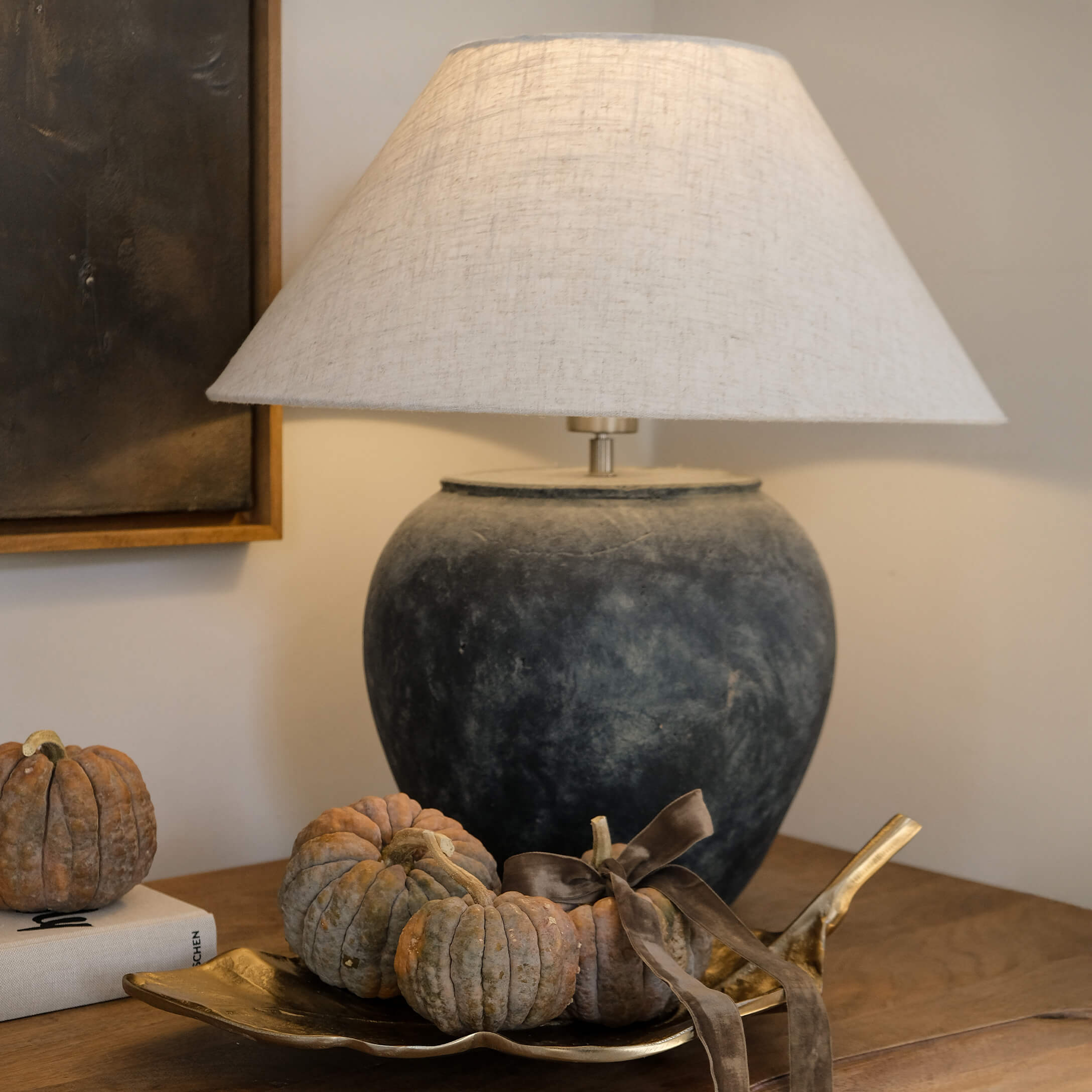 Tischlampe aus dunkelgrauer Keramik mit beigem Lampenschirm und kleinen Kürbissen auf goldfarbenem Tablett