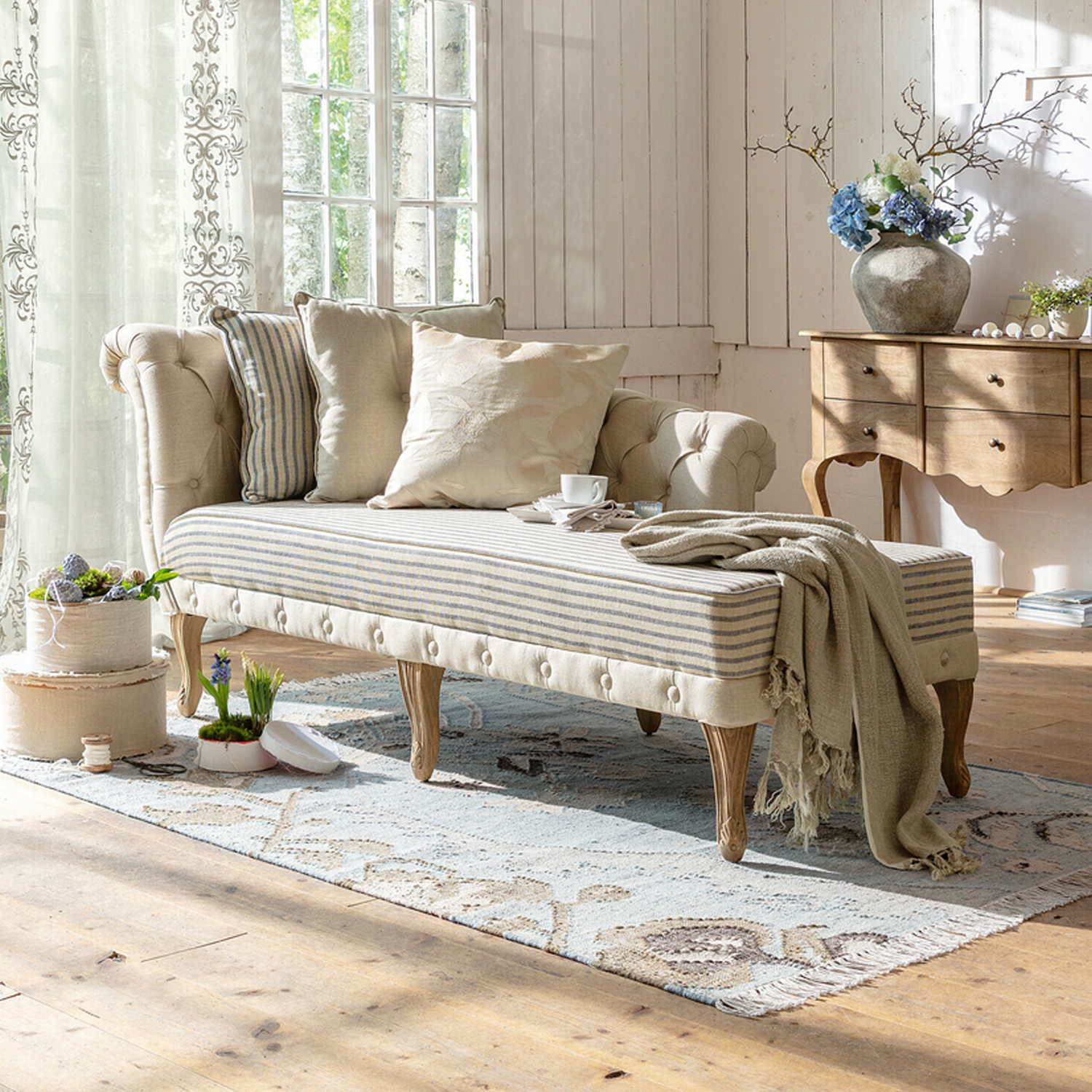 Beige gepolsterte Chaiselongue mit Holzbeinen und hellen Kissen in hellem Wohnzimmer