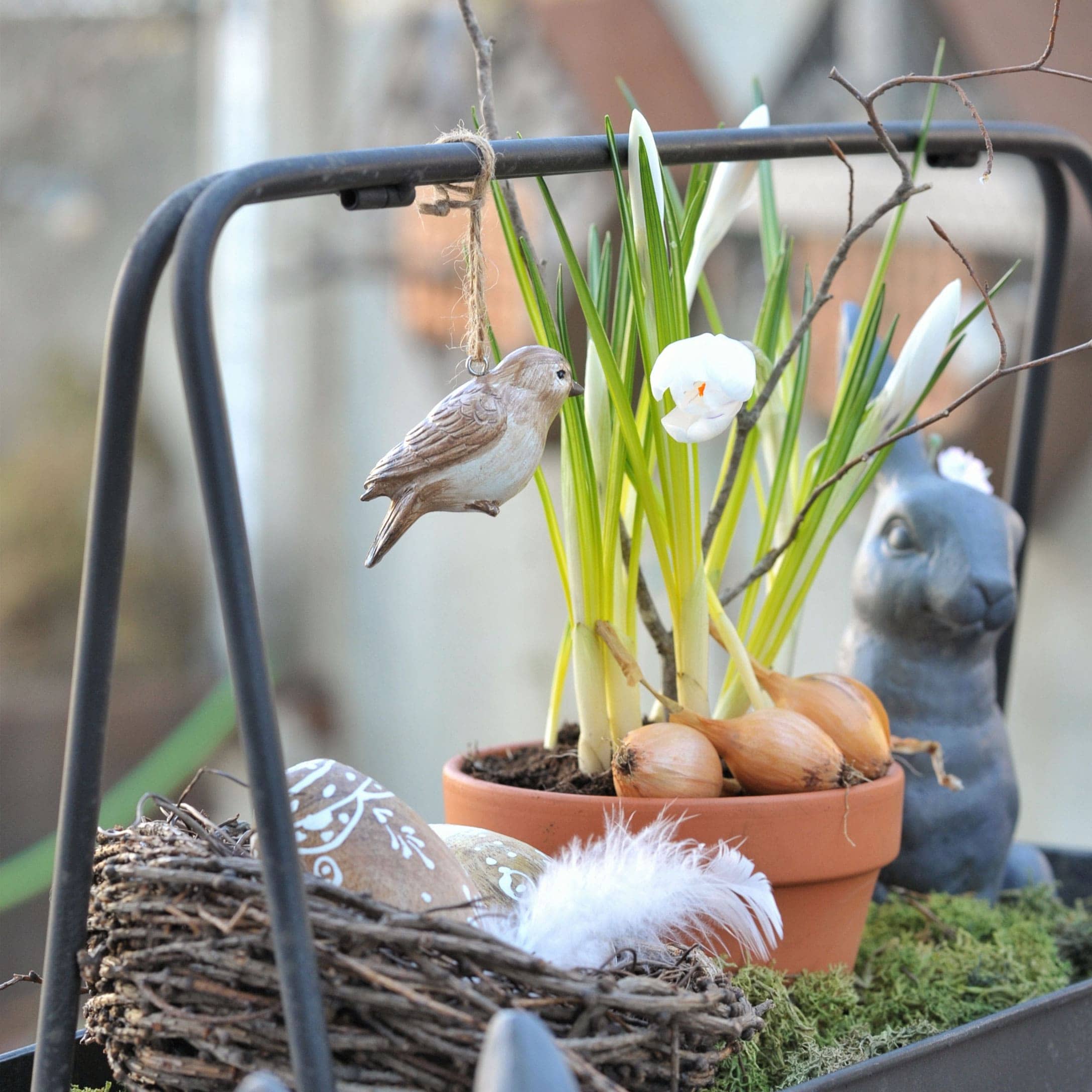 Dekorativer Holzvogel an Blumentopf mit Zwiebeln und weißen Blüten für frühlingshafte Dekoration