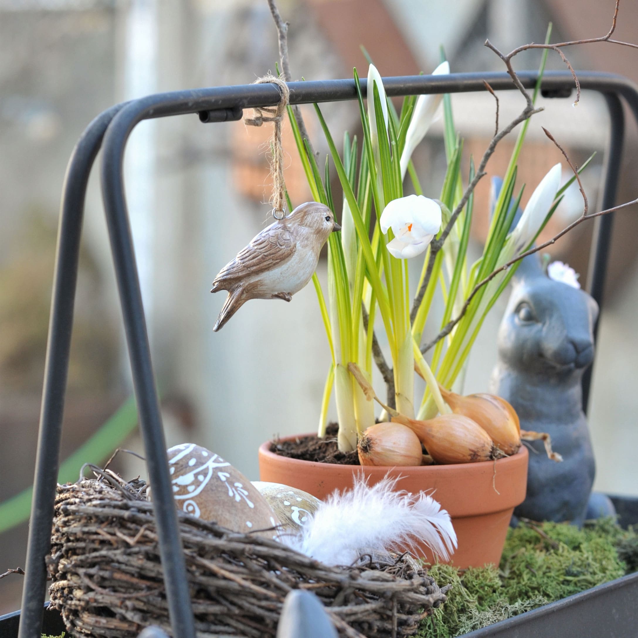 Dekorativer Holzvogel an Blumentopf mit Zwiebeln und weißen Blüten für frühlingshafte Dekoration