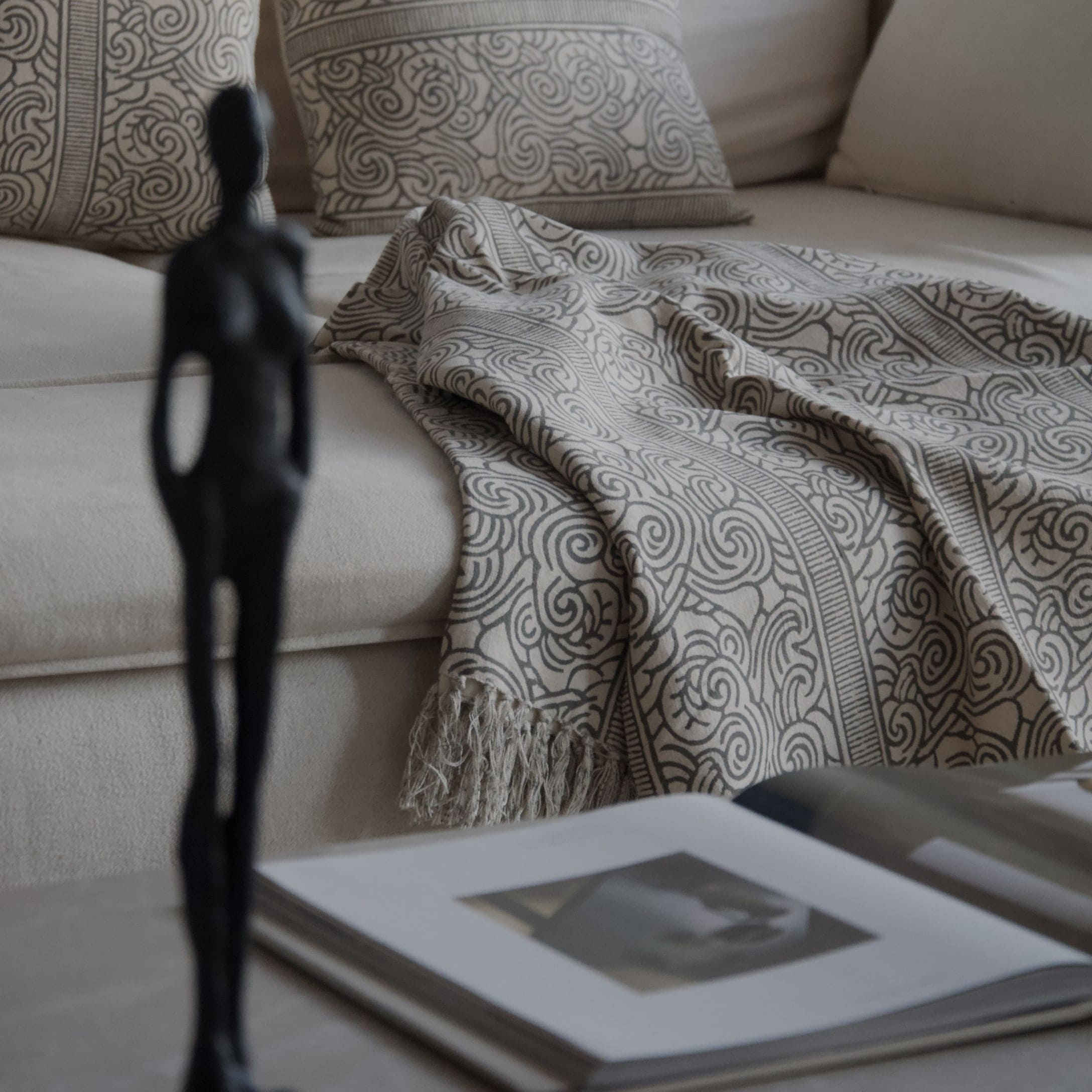 Beige Decke mit grauem Muster und Fransen auf hellem Sofa mit dekorativen Kissen