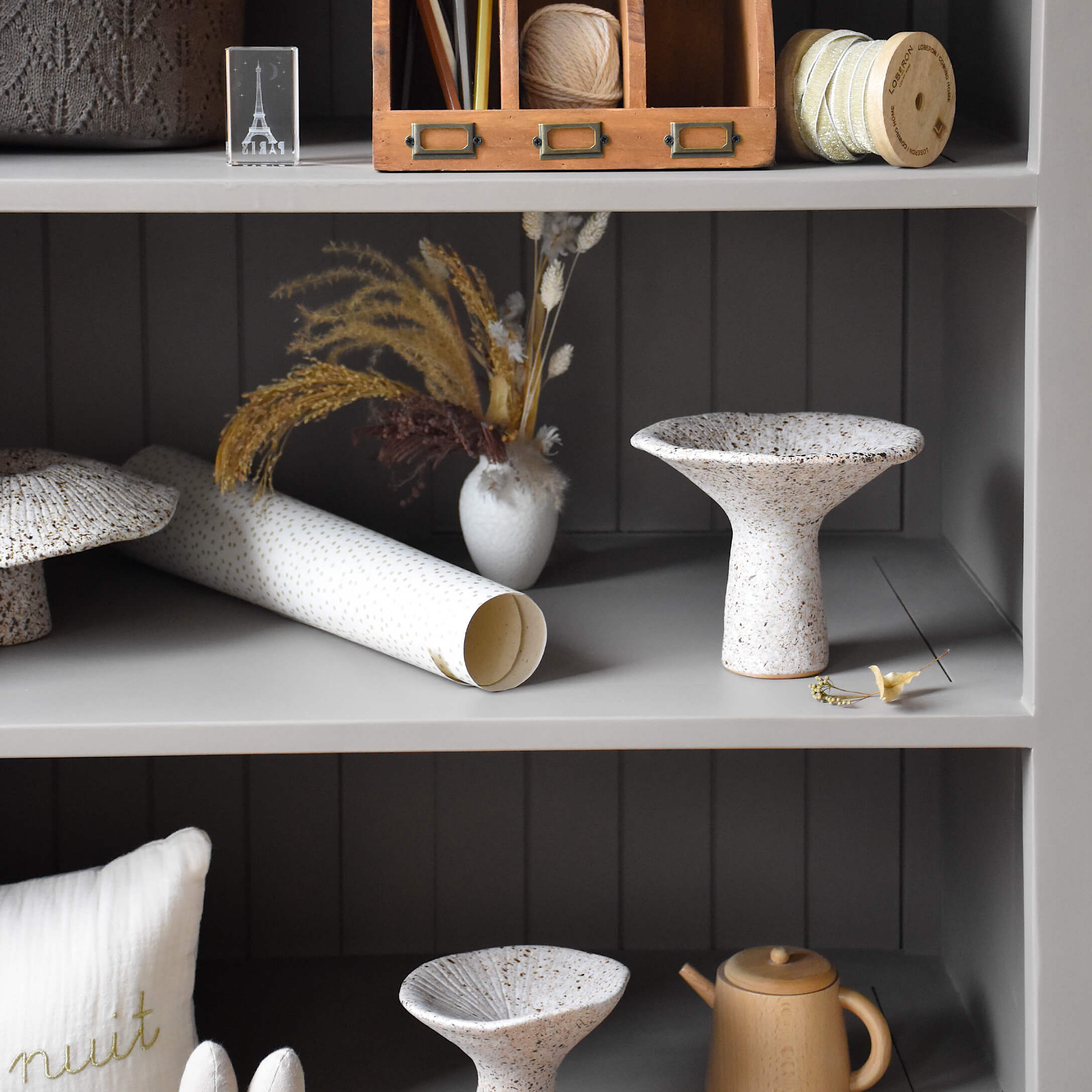 Weiße Keramikschale mit braunen Sprenkeln auf grauem Regal mit Dekoration und Trockenblumen