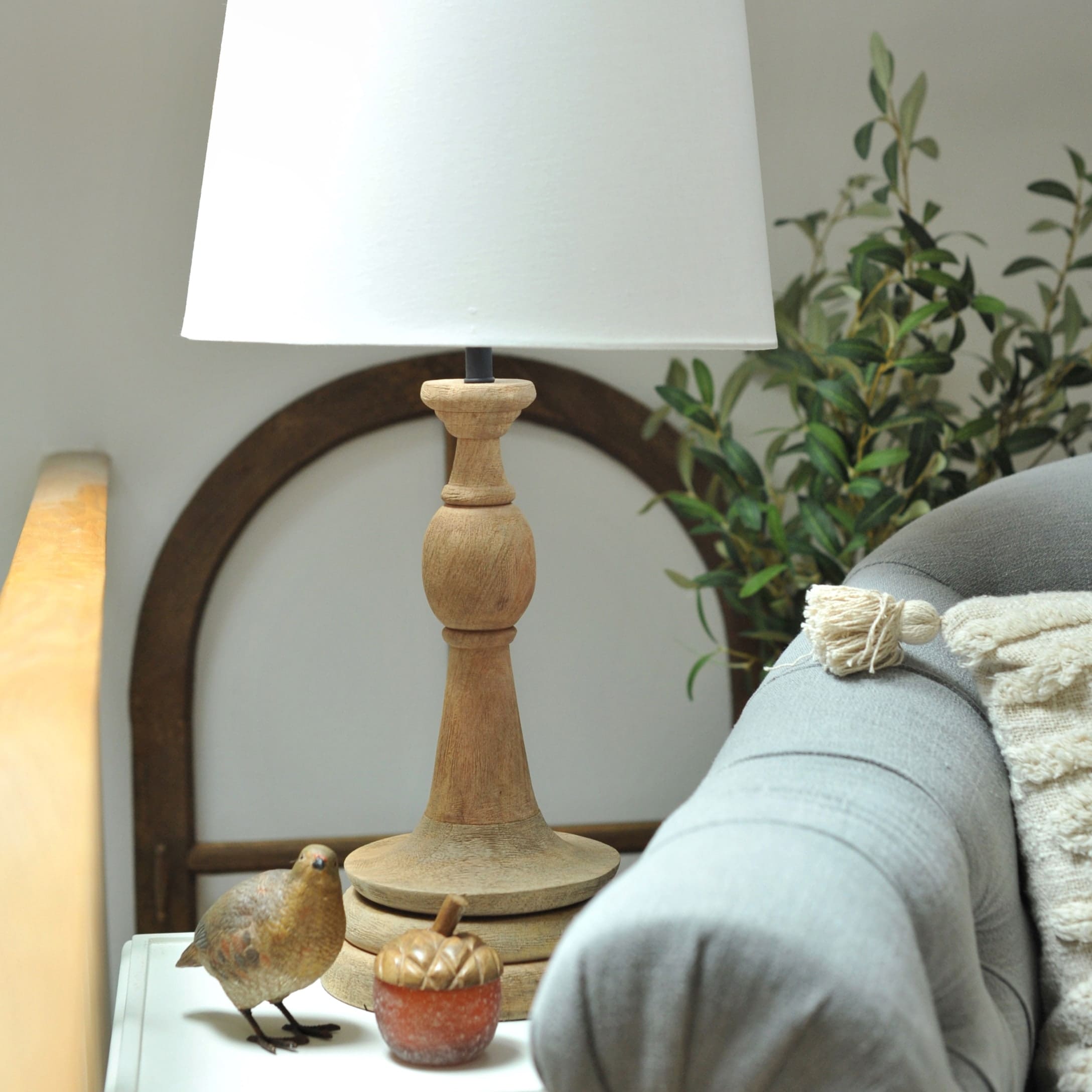 Tischlampe mit Holzfuß und weißem Lampenschirm auf Beistelltisch neben grauem Sofa und Dekoration