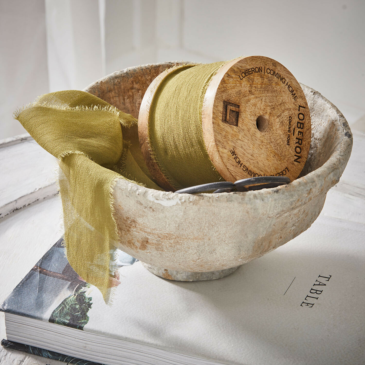 Band Lunebrook Natürliche Steinschale mit grünem Stoff und Holzspule auf einem Buch zum Thema Tisch