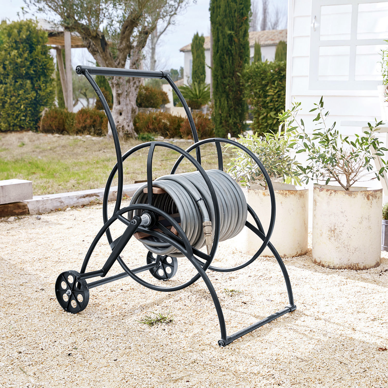 Schlauchwagen Middleby Schwarzer Metall-Wagen mit grauem Gartenschlauch auf Kiesfläche im Garten