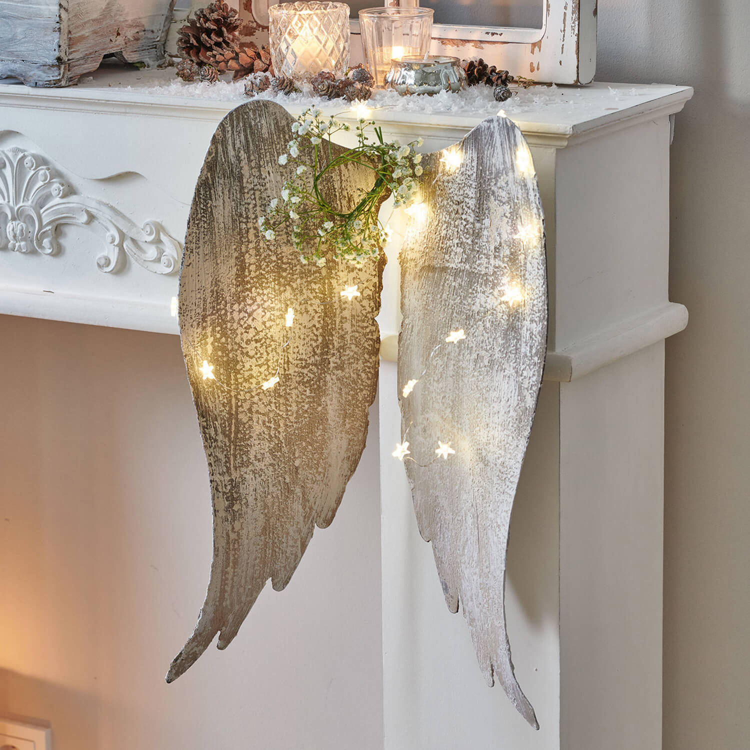 Dekorative weiße Holz-Engelsflügel mit LED-Lichterkette und grünen Zweigen als Wanddeko
