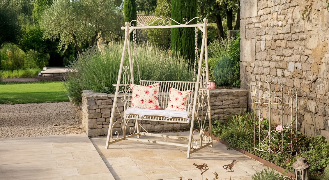 Weiße Metall-Gartenschaukel mit rot-weißen Blumenmustern auf Kissen auf Stein-Terrasse