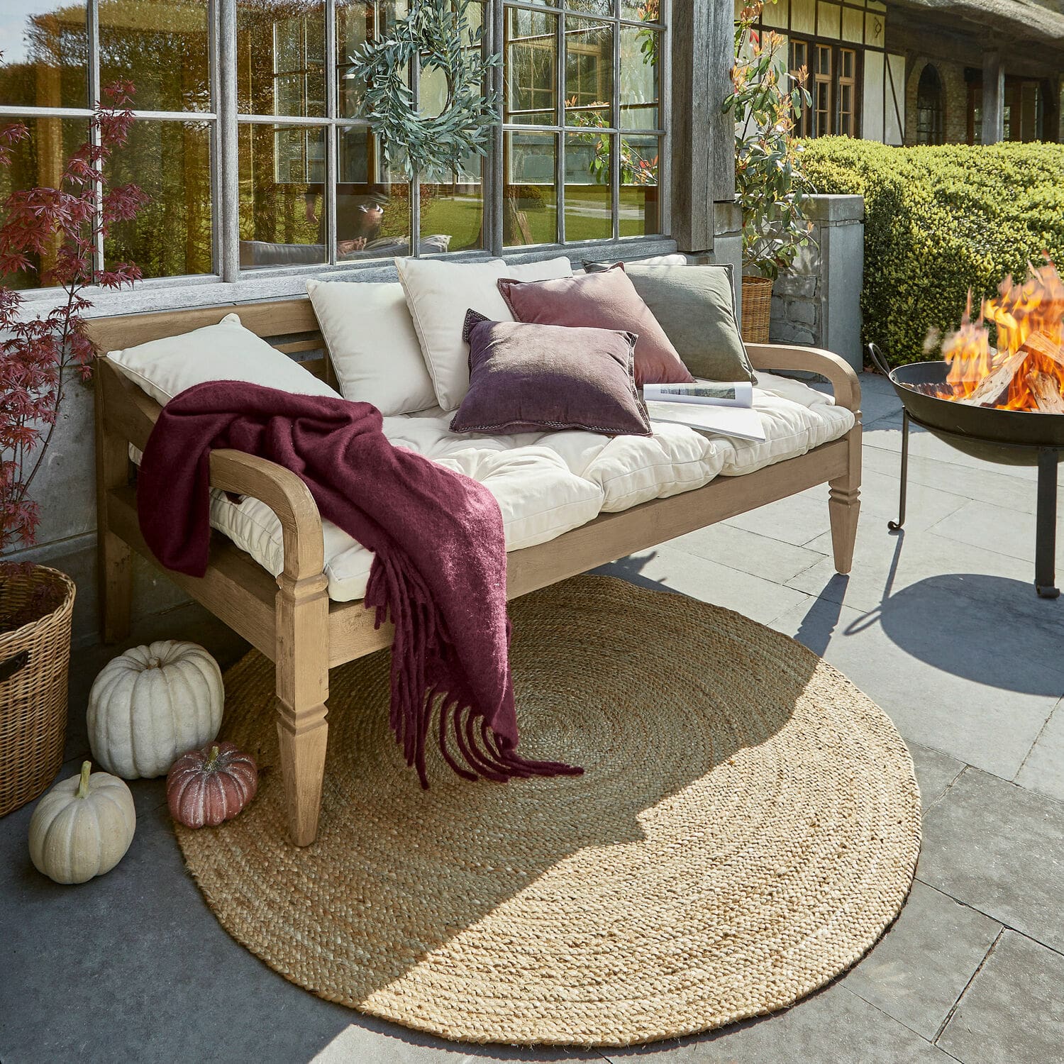 Bank Fairwood Holzbank mit cremefarbenen Kissen und bordeauxroter Decke auf Terrasse mit Jute-Teppich