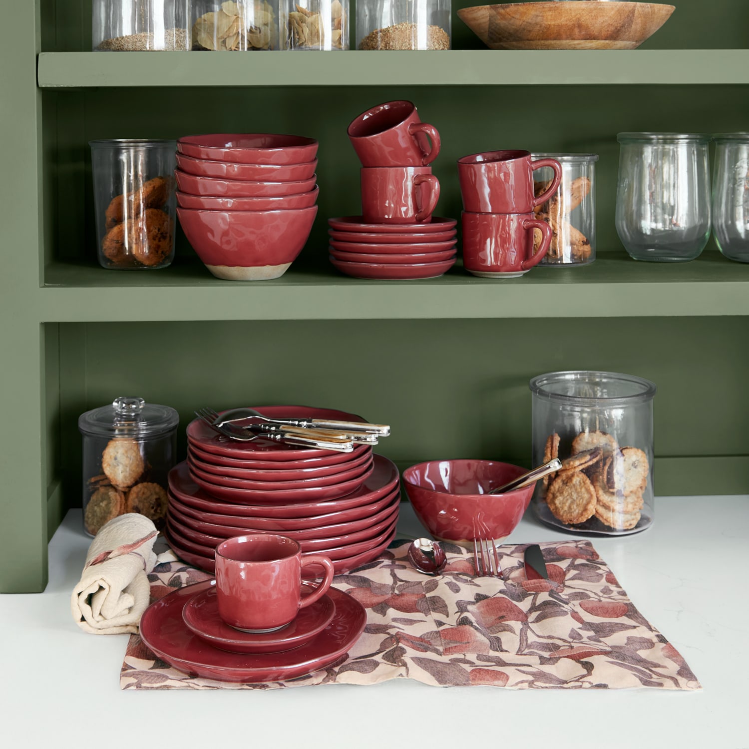 Rotes Keramik-Geschirrset auf grünem Regal mit Keksen in Glasbehältern