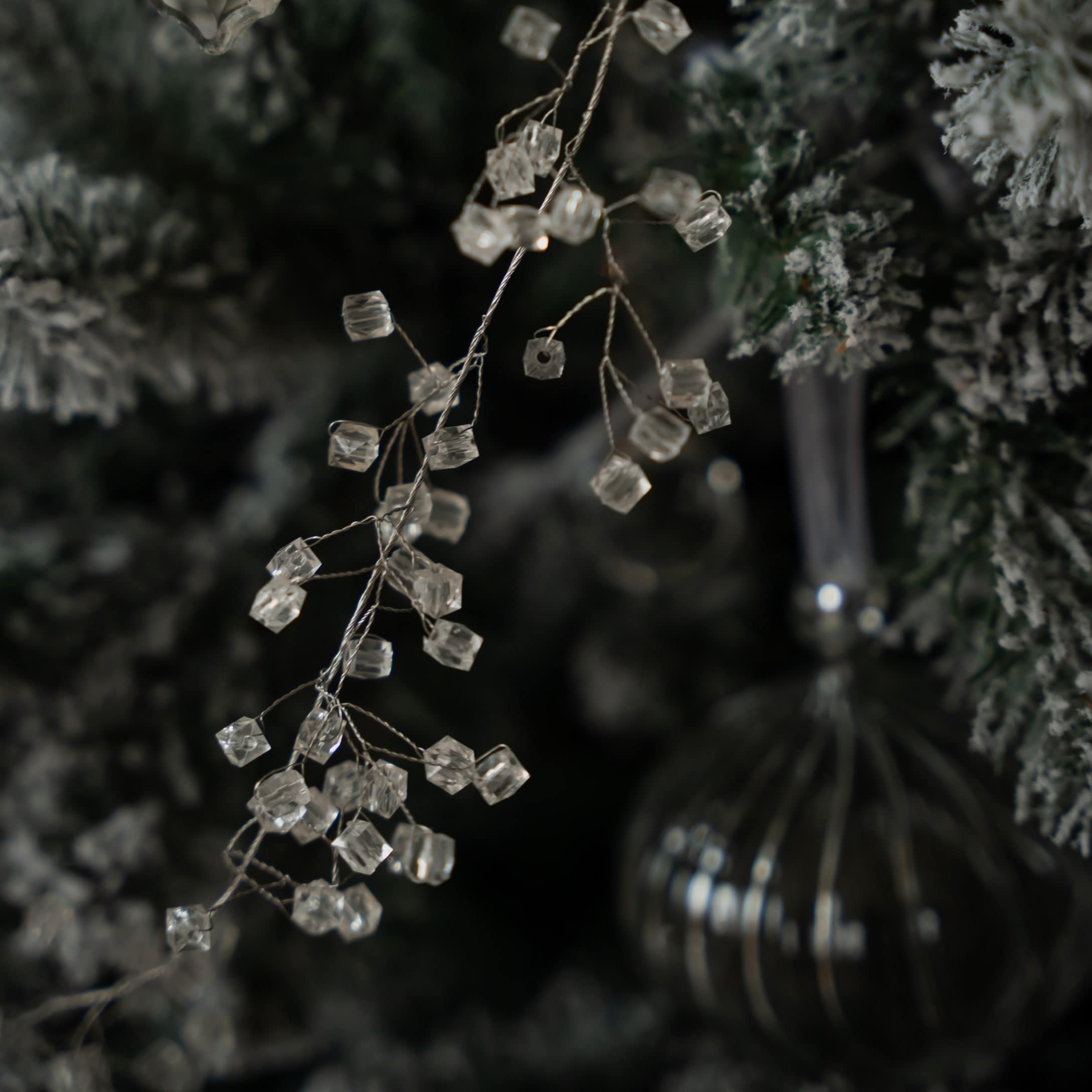 Dekorative transparente Kristallperlen an Zweig vor künstlichem, schneebedecktem Weihnachtsbaum