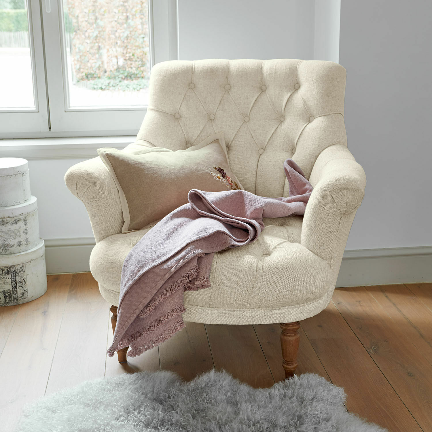 Sessel Rive Dorée Beiger Polstersessel mit Holzbeinen, rosa Decke und grauem Lammfellteppich auf Holzboden