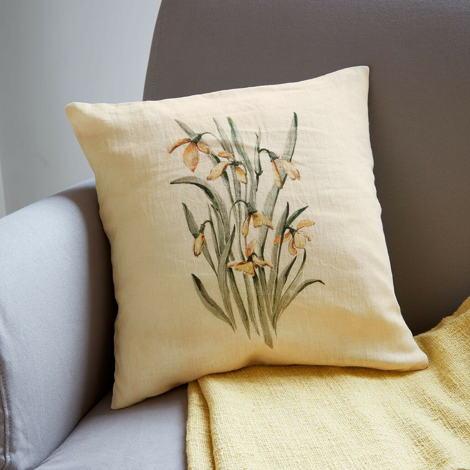 Beige Leinenkissen mit gelbem Blumenmotiv auf grauem Sofa mit gelber Decke