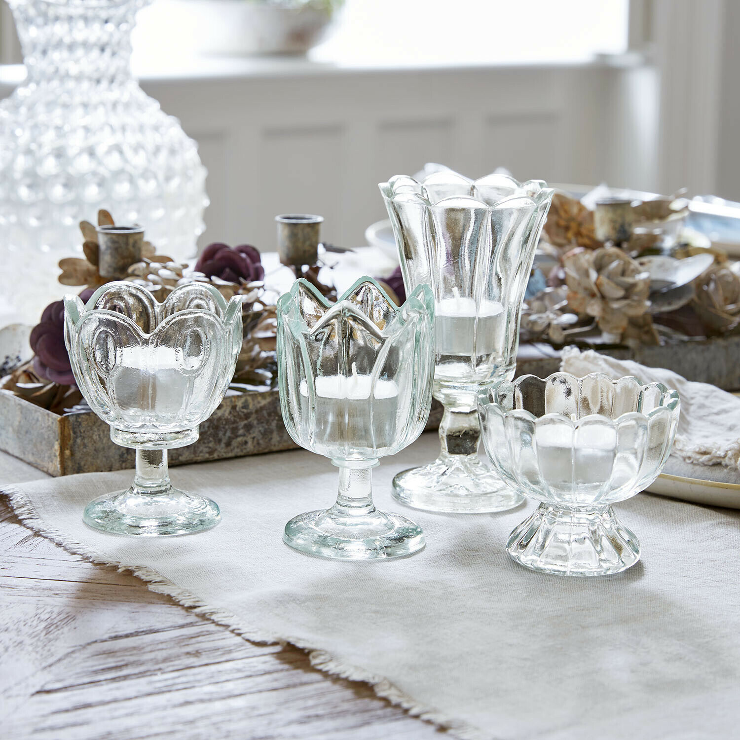 Windlicht 4er Set Amisette Set aus vier transparenten Glas-Teelichthaltern in verschiedenen Formen auf hellem Tuch