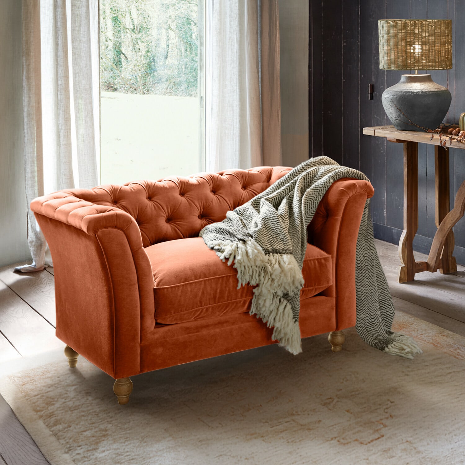 Oranger Samt-Chesterfield-Sofa mit grauem Plaid in gemütlichem Wohnzimmer mit Lampe und Holztisch