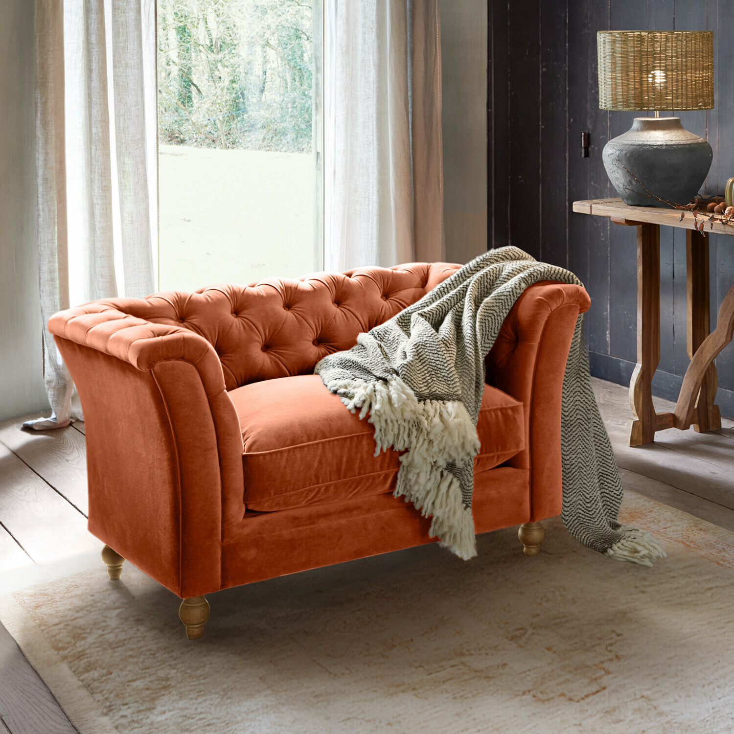 Sofa Clères Oranger Samt-Chesterfield-Sofa mit grauem Plaid in gemütlichem Wohnzimmer mit Lampe und Holztisch