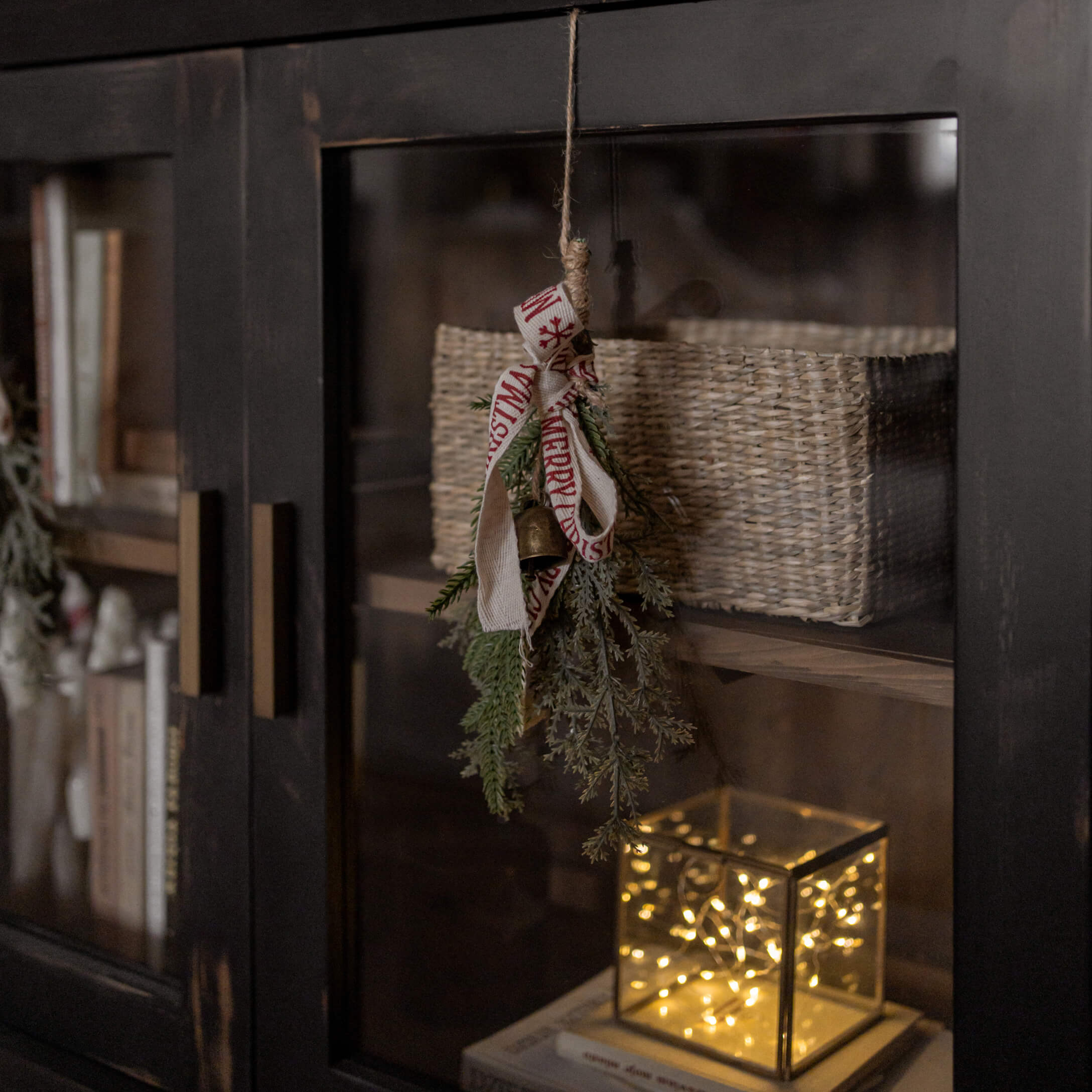 Weihnachtsdekoration mit grünen Zweigen, Glocke und Band an schwarzem Schrank mit Korb und LED-Licht