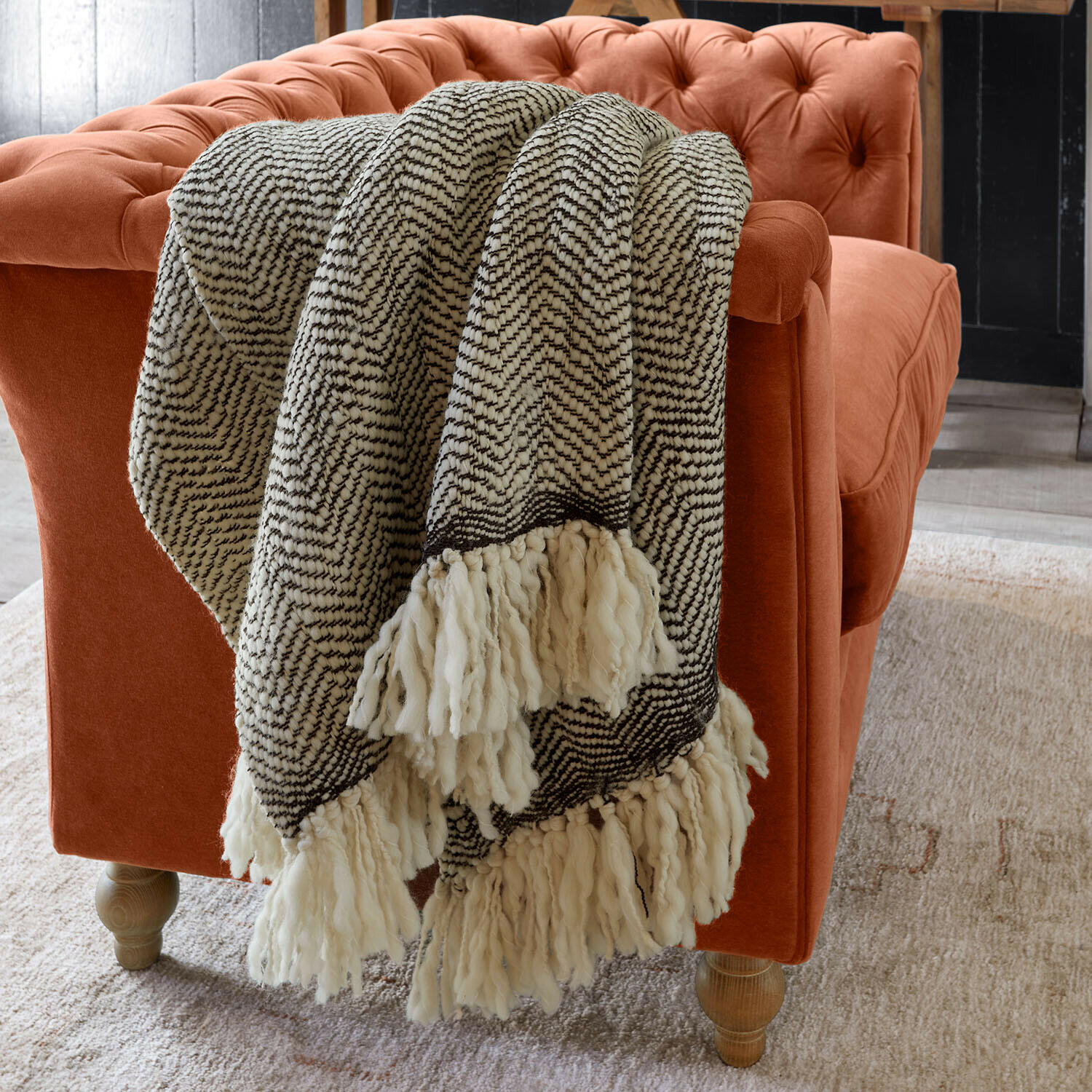 Plaid Kerenza Weiche schwarz-weiße Kuscheldecke mit Fransen auf orangefarbenem Samtsofa im Wohnzimmer