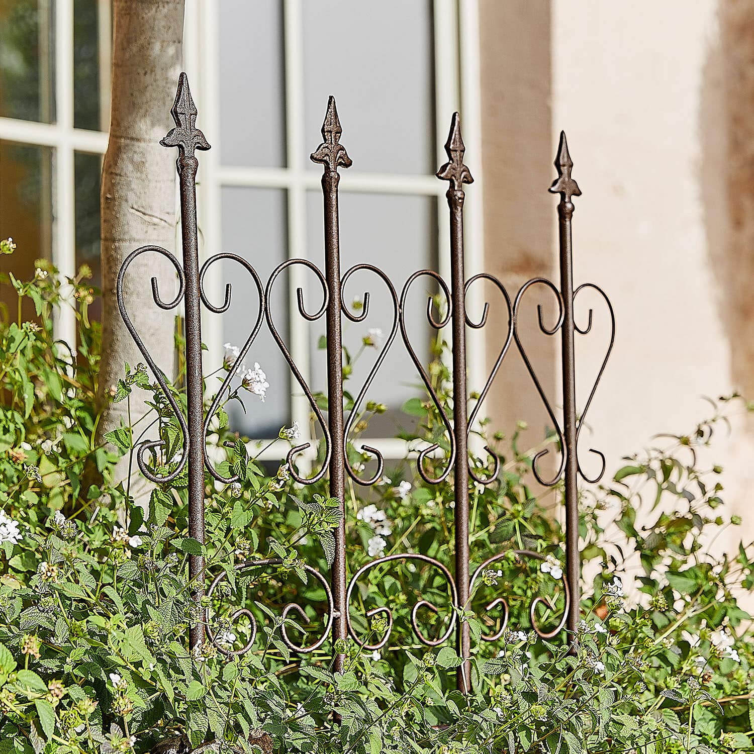 Rankhilfe Nectarise Dekorativer Gartenzaun aus rostbraunem Metall mit Herzmotiv, umgeben von grünen Pflanzen und weißen Blüten