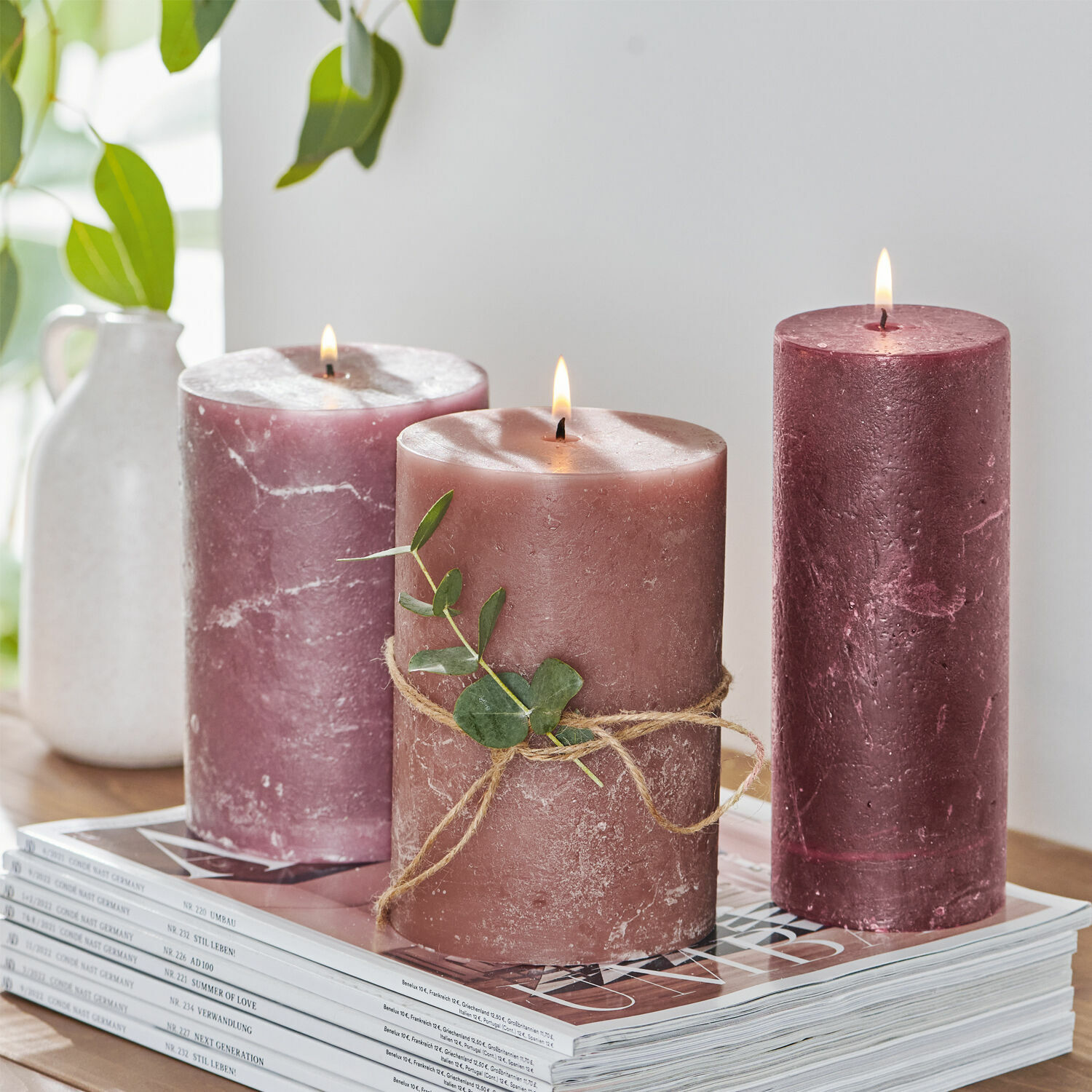 Kerze 3er Set Salis Drei rosa Kerzen aus Wachs mit grünem Blatt auf einem Stapel Zeitschriften, Wohnaccessoire