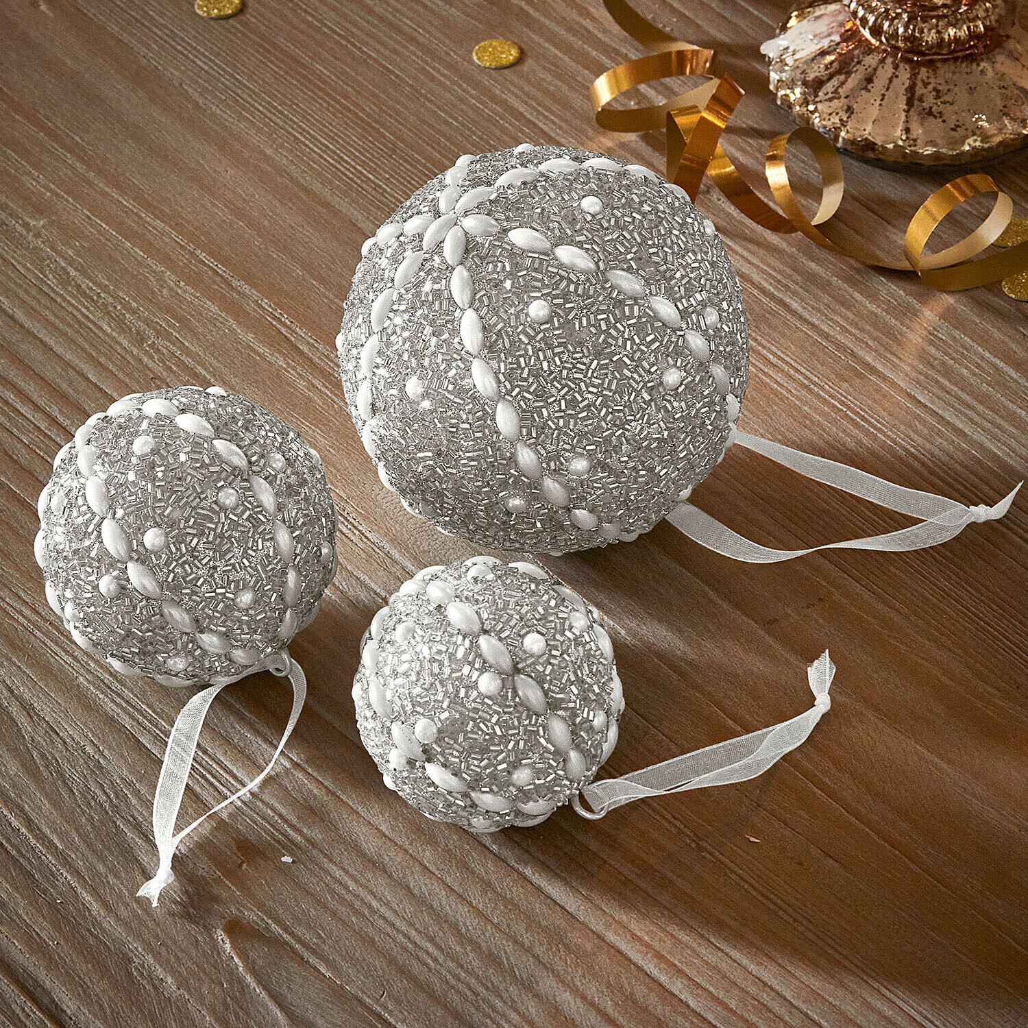Weihnachtskugel 3er Set Maelvik Set aus drei silbernen Weihnachtskugeln mit Perlenbesatz und Bändern auf Holztisch
