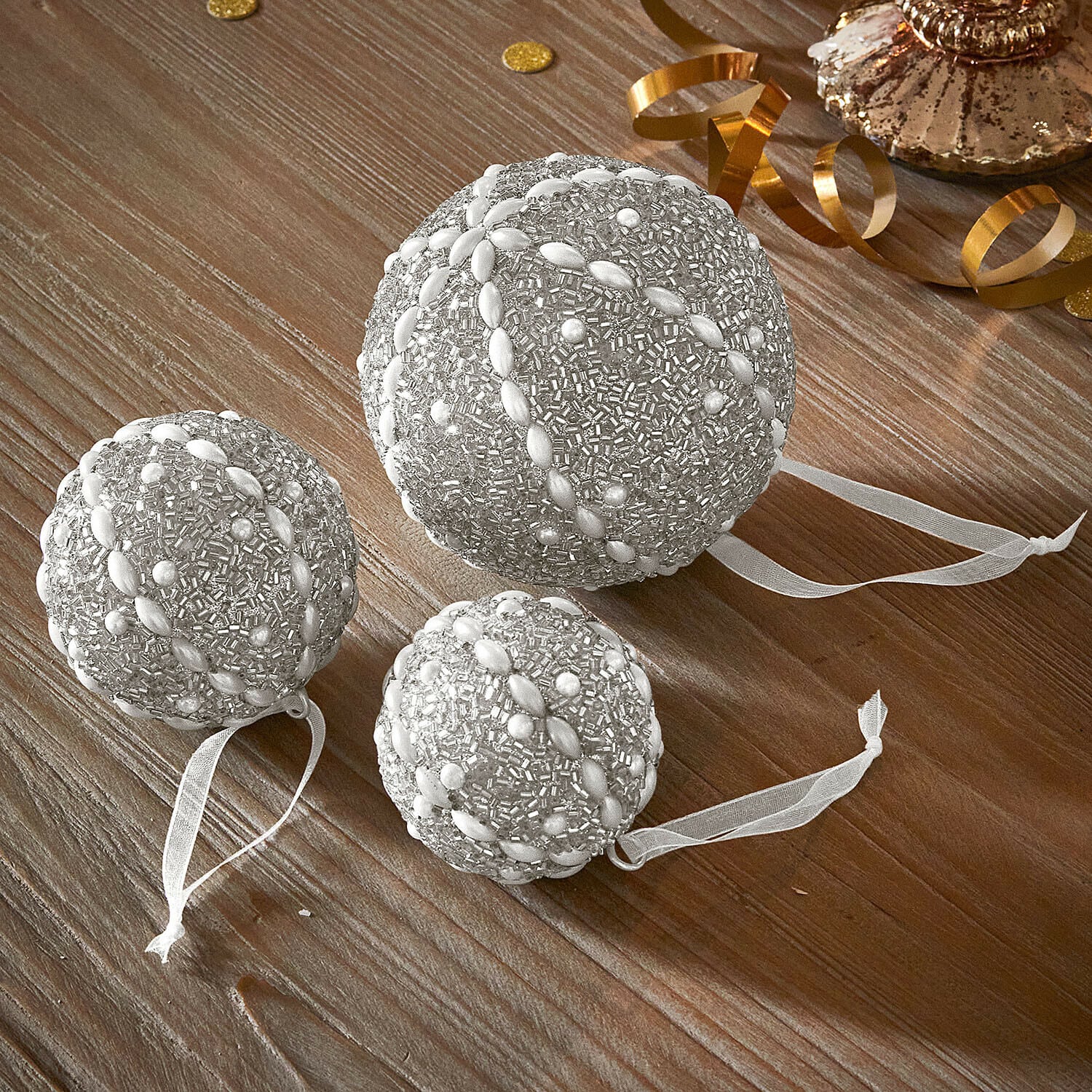 Weihnachtskugel 3er Set Maelvik Set aus drei silbernen Weihnachtskugeln mit Perlenbesatz und Bändern auf Holztisch