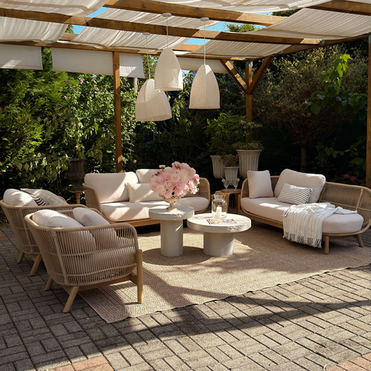 Beige Gartenmöbel-Set mit Polstern und Holzrahmen unter Pergola mit weißen Hängelampen