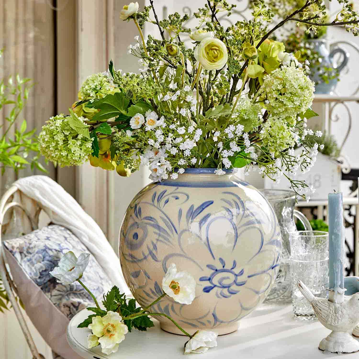 Runde Keramikvase mit blauem Blumenmuster und grün-weißen Blumen auf einem Tisch