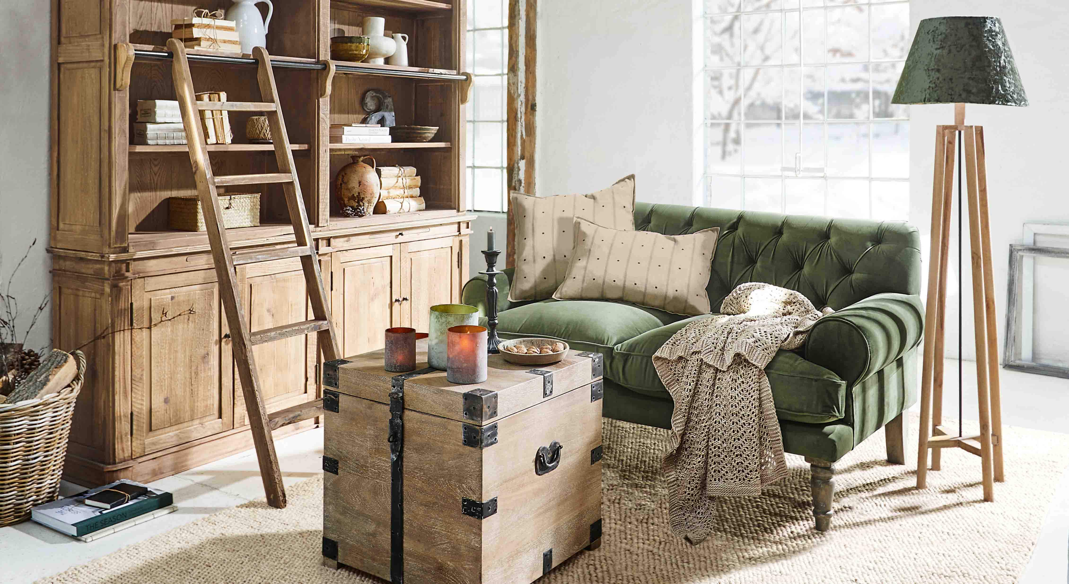 Gemütliches Wohnzimmer mit grünem Samtsofa, Holzschrank und Stehlampe aus Naturholz