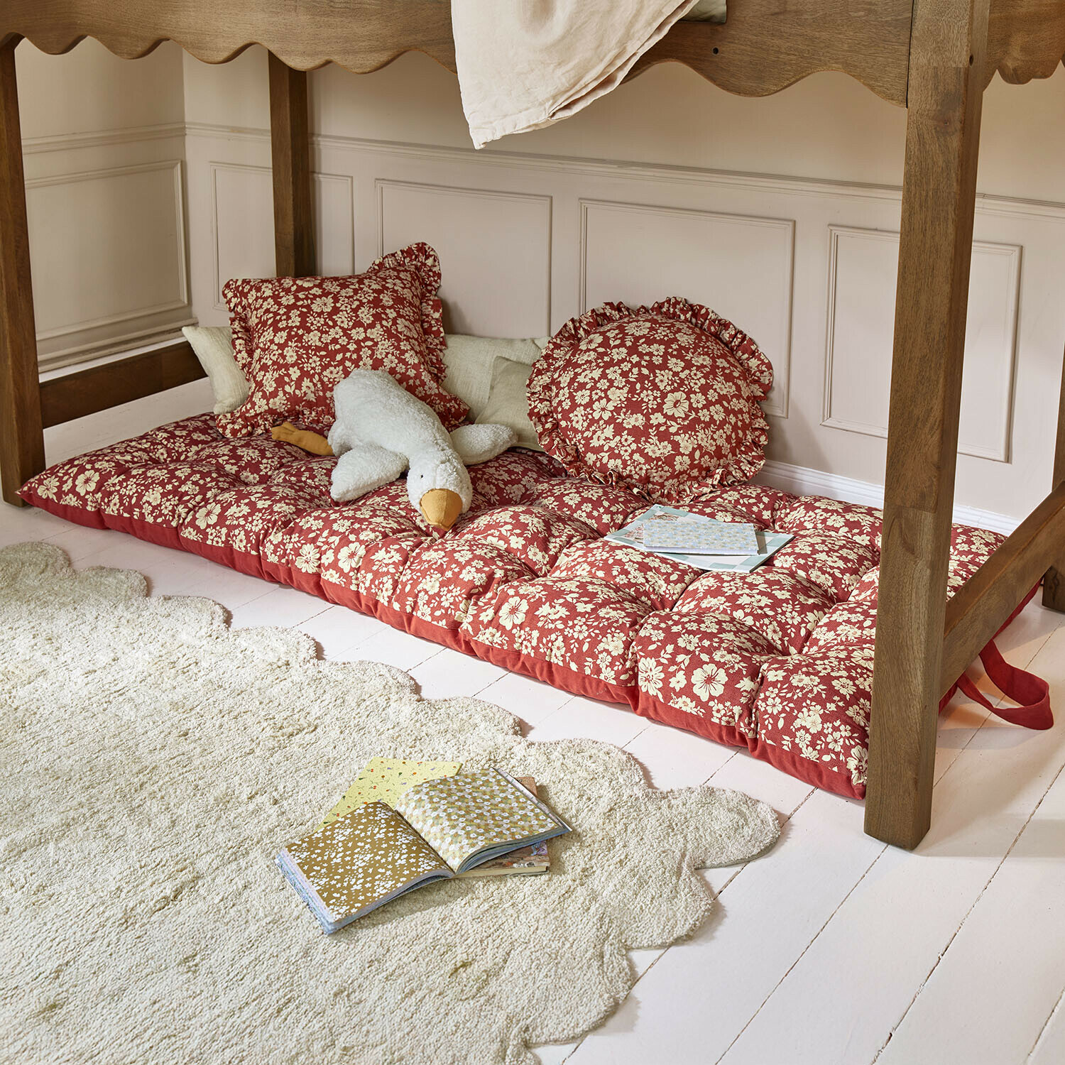 Spielmatratze Frambelle Rotes, floral gemustertes Sitzkissen mit Kissen unter einem Holztisch, Plüschtier und Bücher auf dem Boden