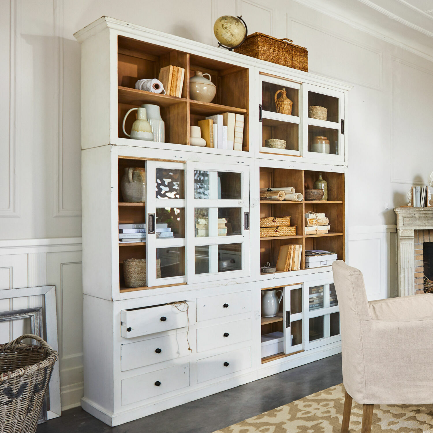 Schrank Dubberly Weißer Holzschrank mit Glastüren und Schubladen im Vintage-Stil, dekoriert mit Büchern und Körben