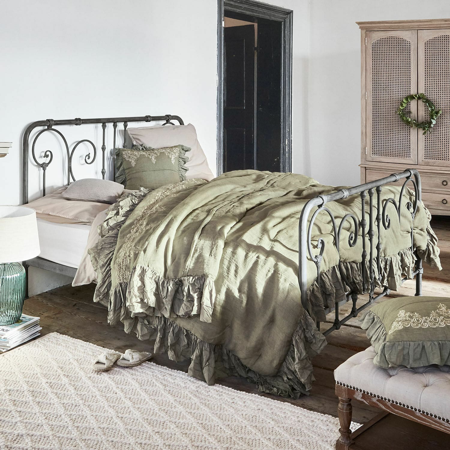 Bett Genouillé Metallbett mit grüner Leinenbettwäsche und Rüschen im rustikalen Schlafzimmer