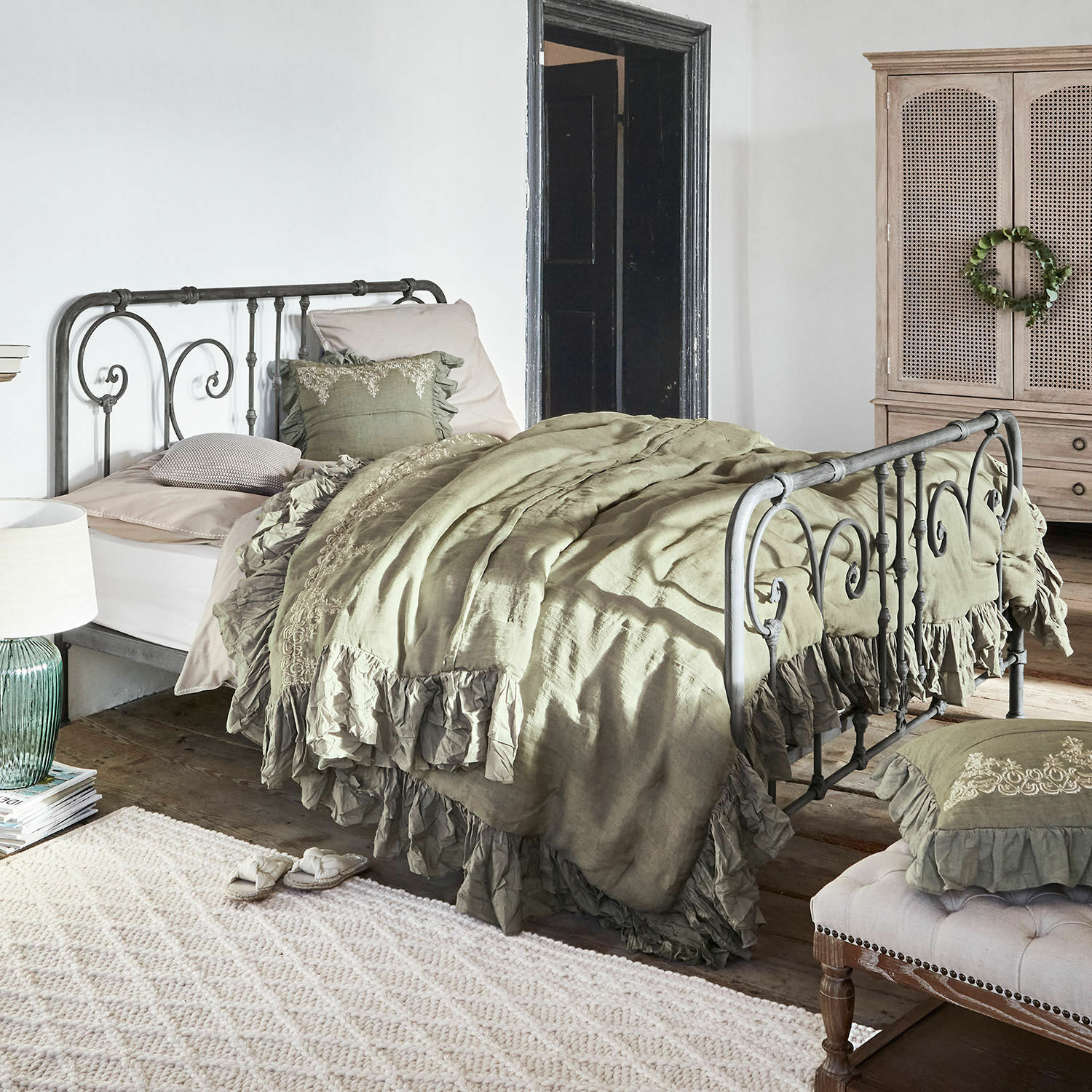 Bett Genouillé Metallbett mit grüner Leinenbettwäsche und Rüschen im rustikalen Schlafzimmer