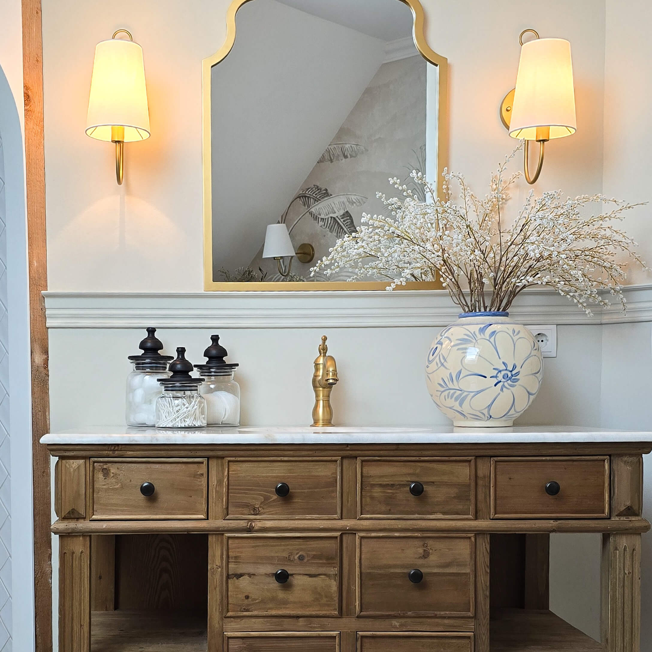 Holzkommode mit Marmorplatte, goldfarbenem Wasserhahn und blau-weißem Keramikvase mit Blumen