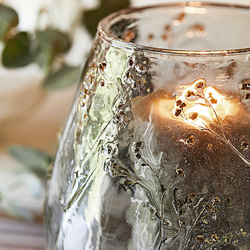 Glaswindlicht mit floraler Reliefdekoration und warmem Kerzenlicht als Wohnaccessoire