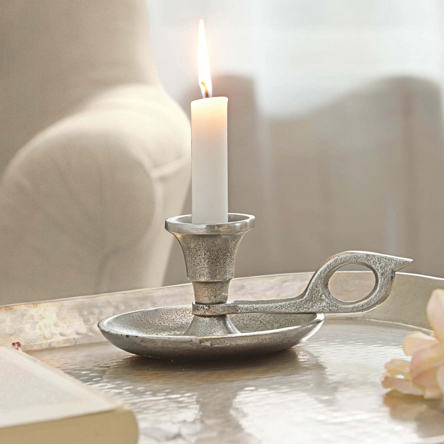 Silberfarbener Metall-Kerzenhalter mit weißer brennender Kerze auf dekorativem Tisch