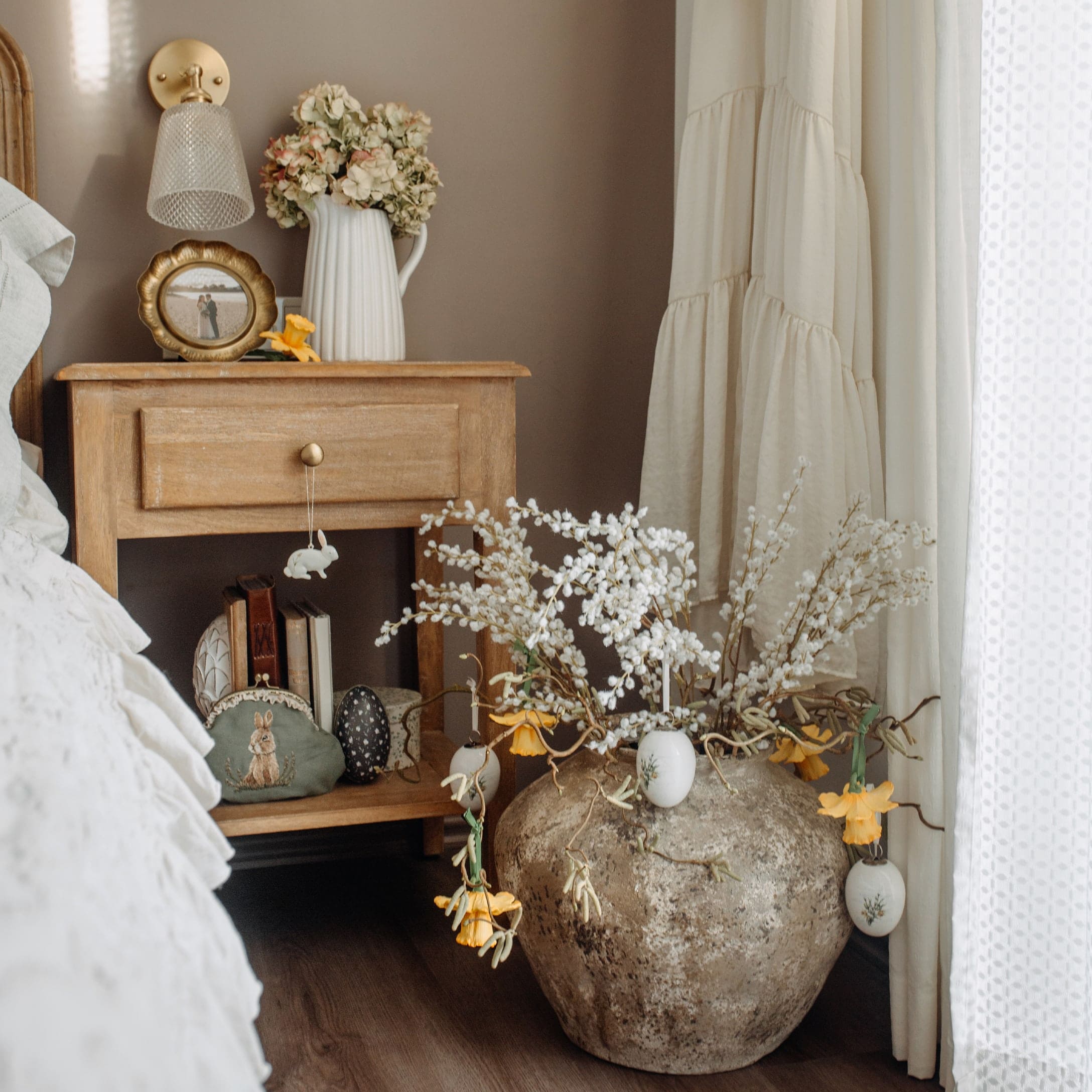 Rustikaler Nachttisch aus Holz mit Osterdekorationen und großem Steinvase mit Blumen