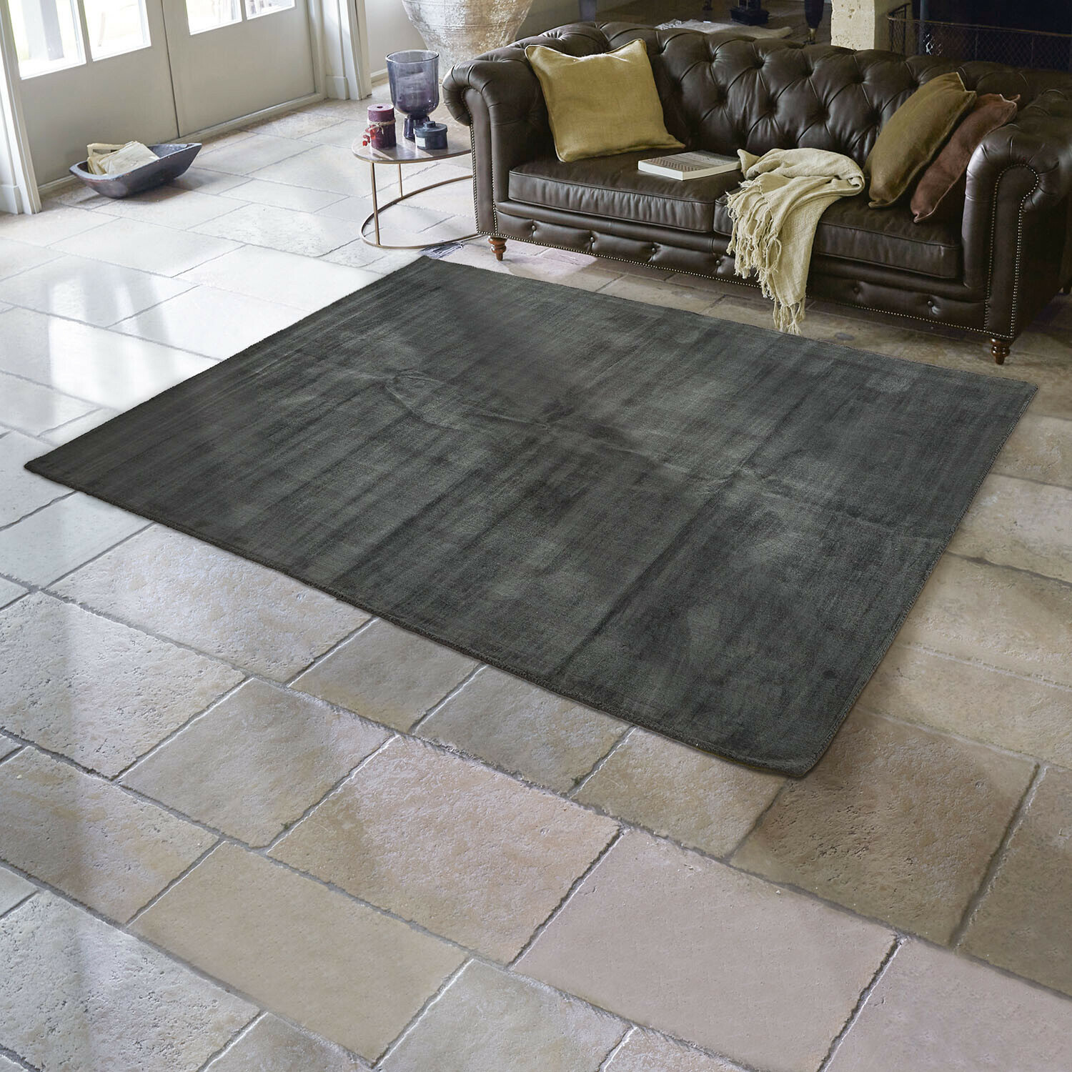 Dunkelgrauer Teppich aus weichem Material auf Steinboden im Wohnzimmer mit braunem Ledersofa