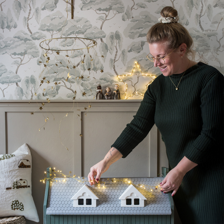Frau schmückt graue Holzkiste mit Stern-Lichterkette in gemütlichem Raum mit Waldtapete