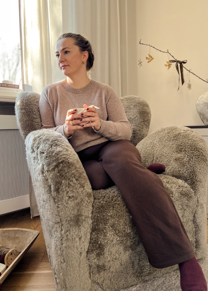 Frau sitzt entspannt in einem grauen, kuscheligen Sessel aus Fellimitat mit Tasse in der Hand.
