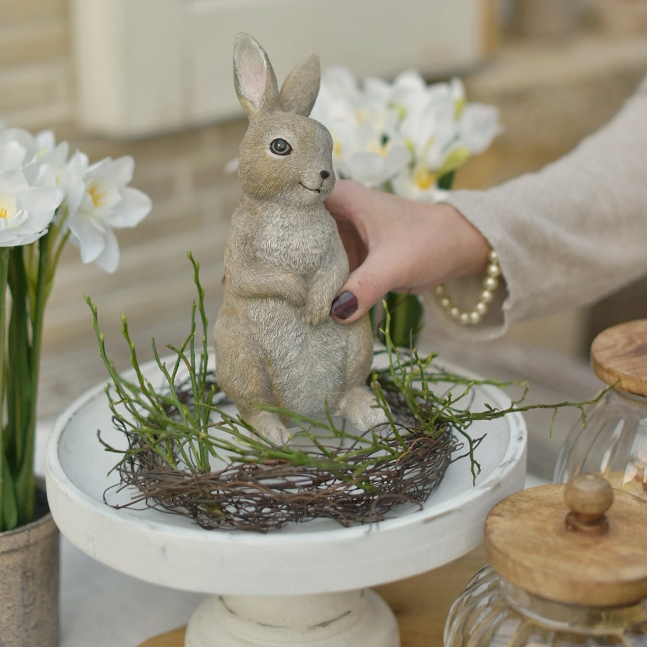 Dekorativer Osterhase in natürlichen Farben auf weißem Podest mit grünen Zweigen