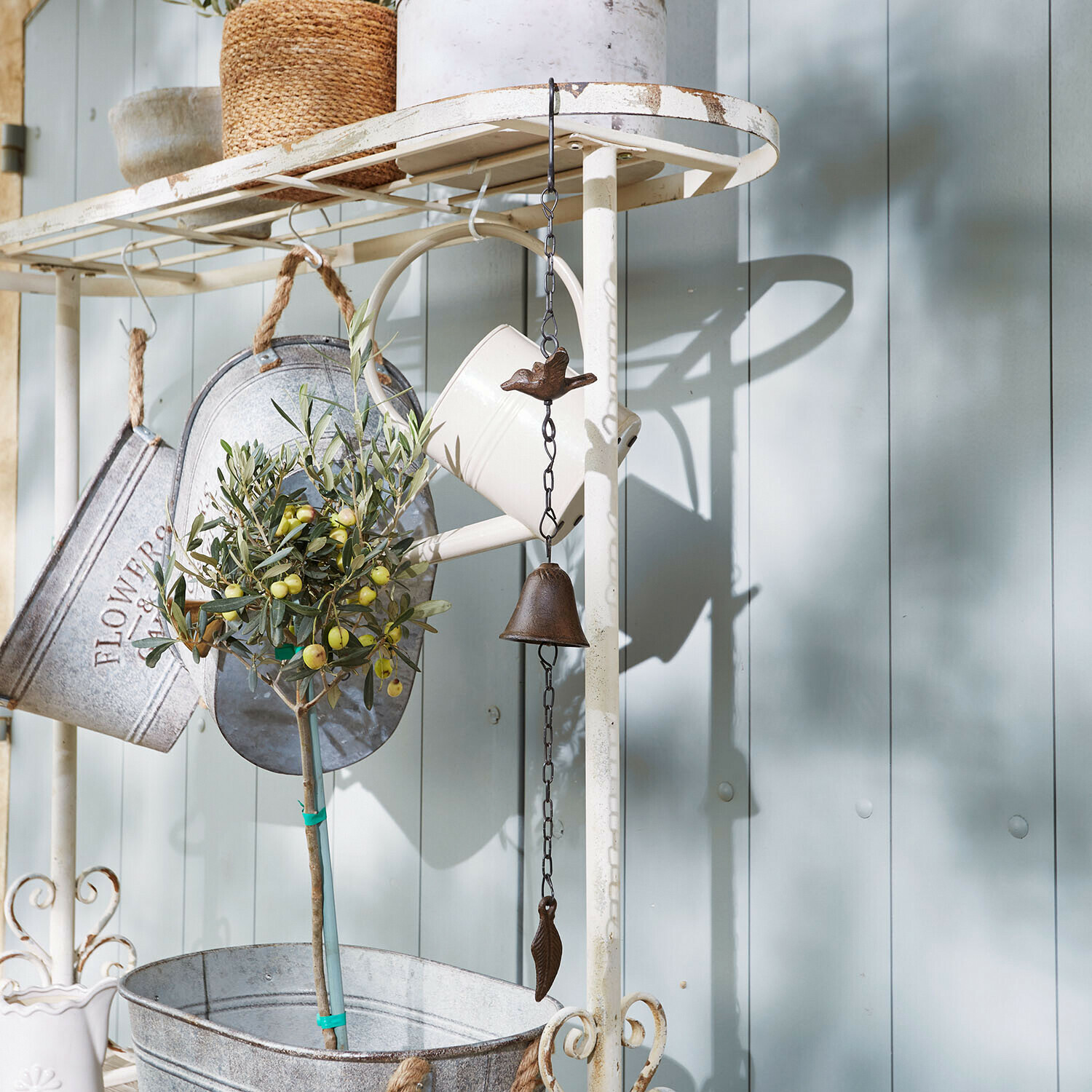 Metall-Gartendekoration mit Glocke und Vogel, weiße Gießkanne und Pflanze im Metalltopf