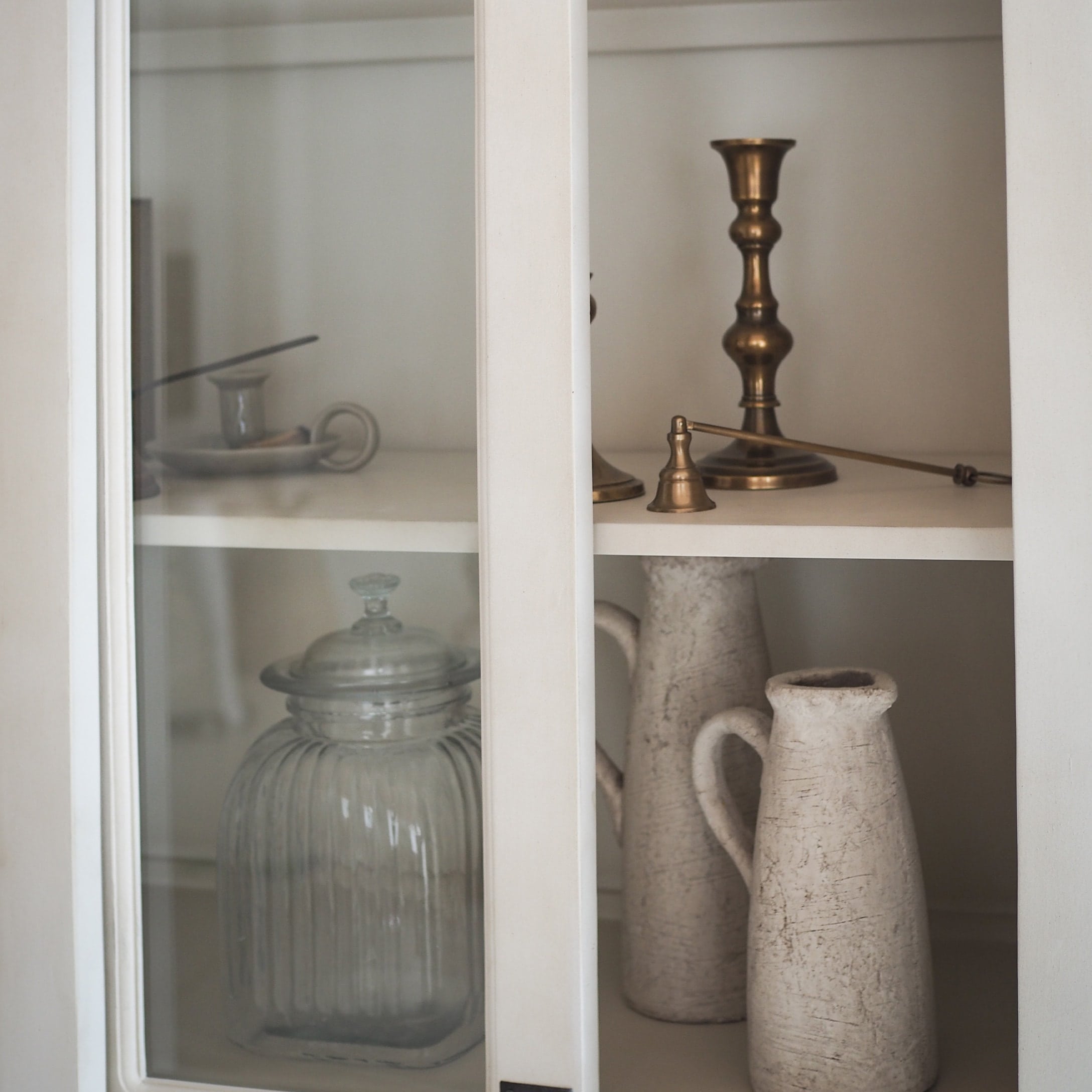Glasbehälter und weiße Keramikkrüge in weißem Schrank mit Messingkerzenhalter und Glocke